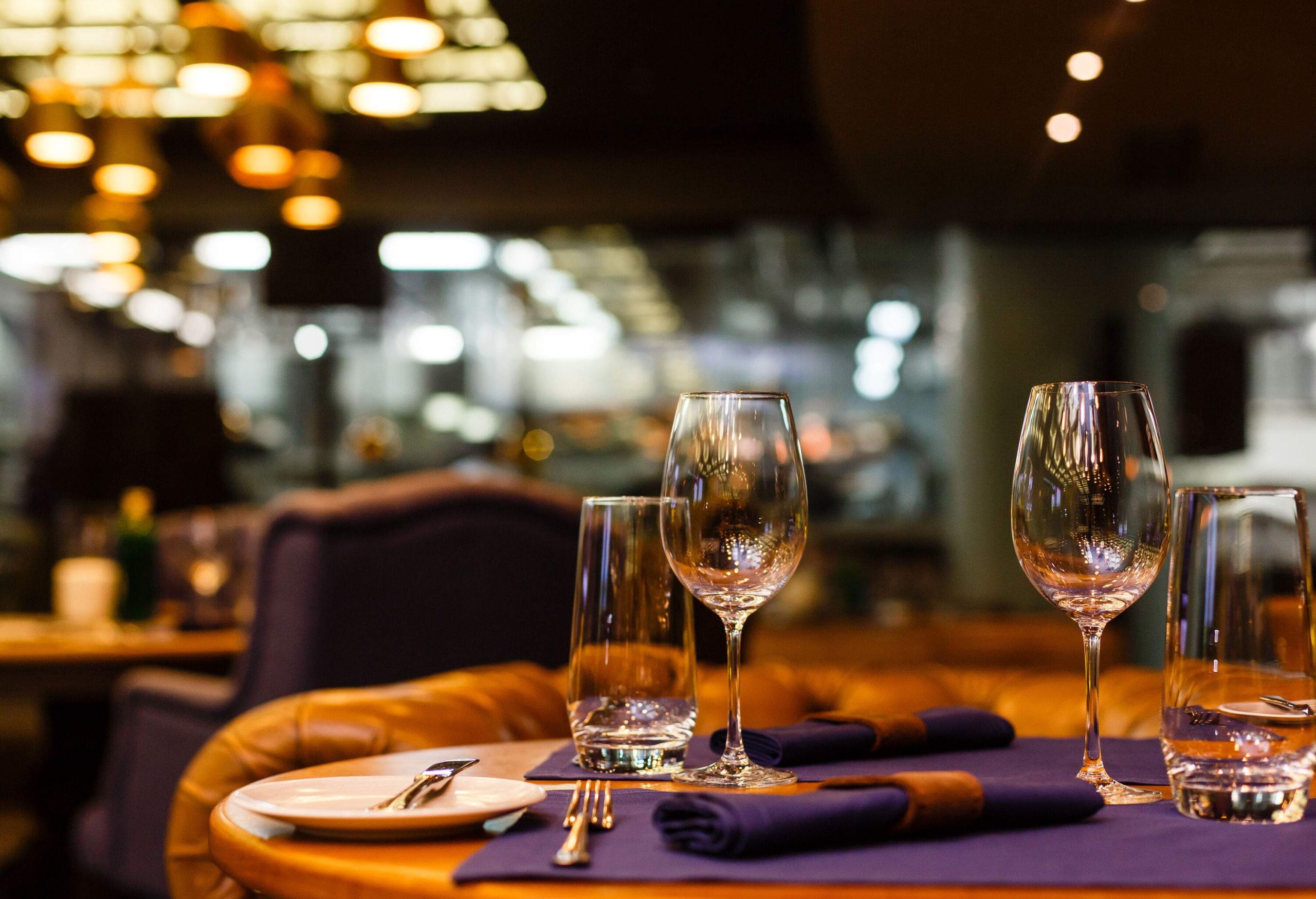 A stylish table setting showcases wine and water glasses adorned with a blue motif, complemented by sleek leather chairs.