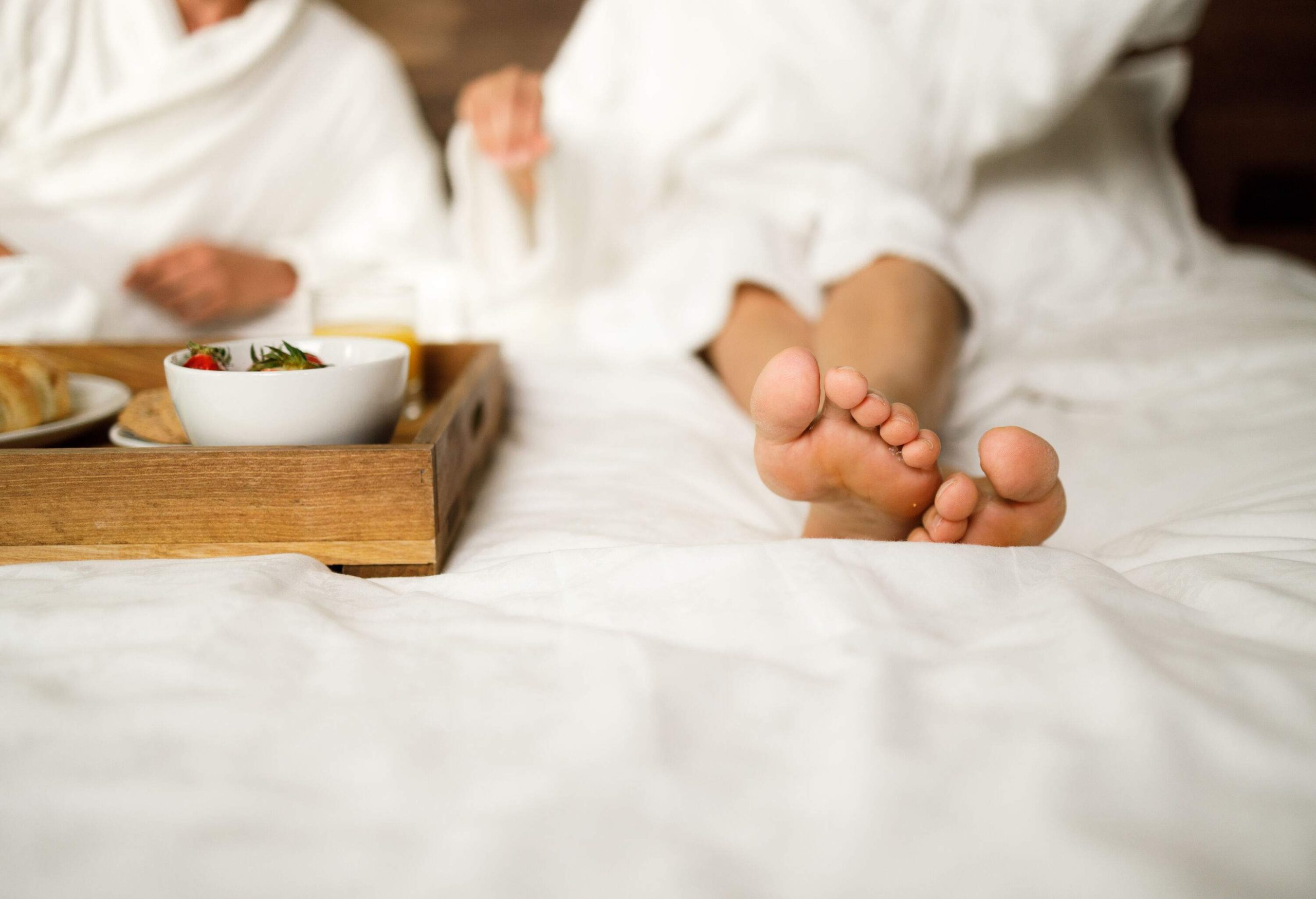 A person in a white bathrobe rests on a bed with their feet exposed.