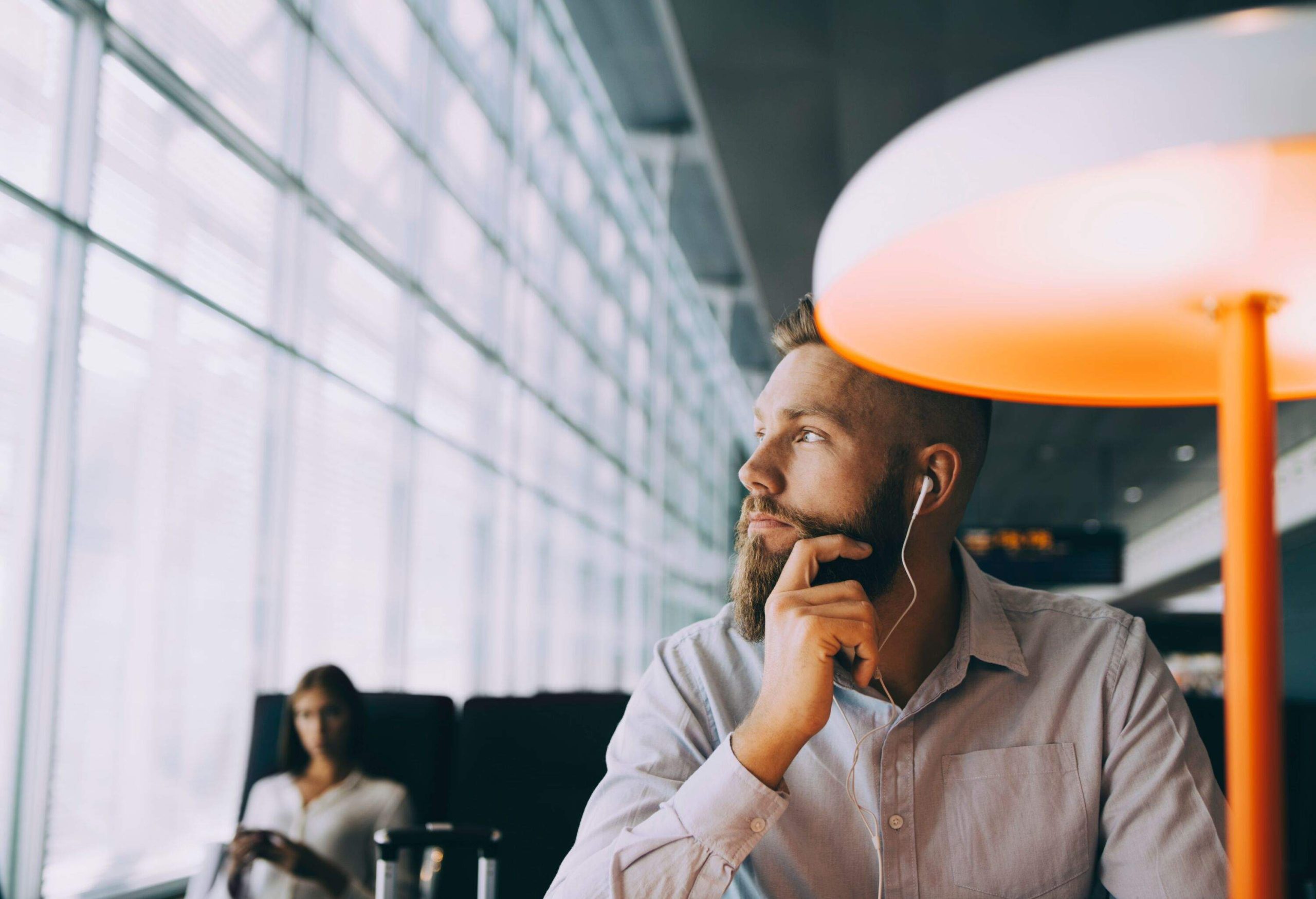 Man wearing earphones sitting at airport terminal by a lamp in lounge