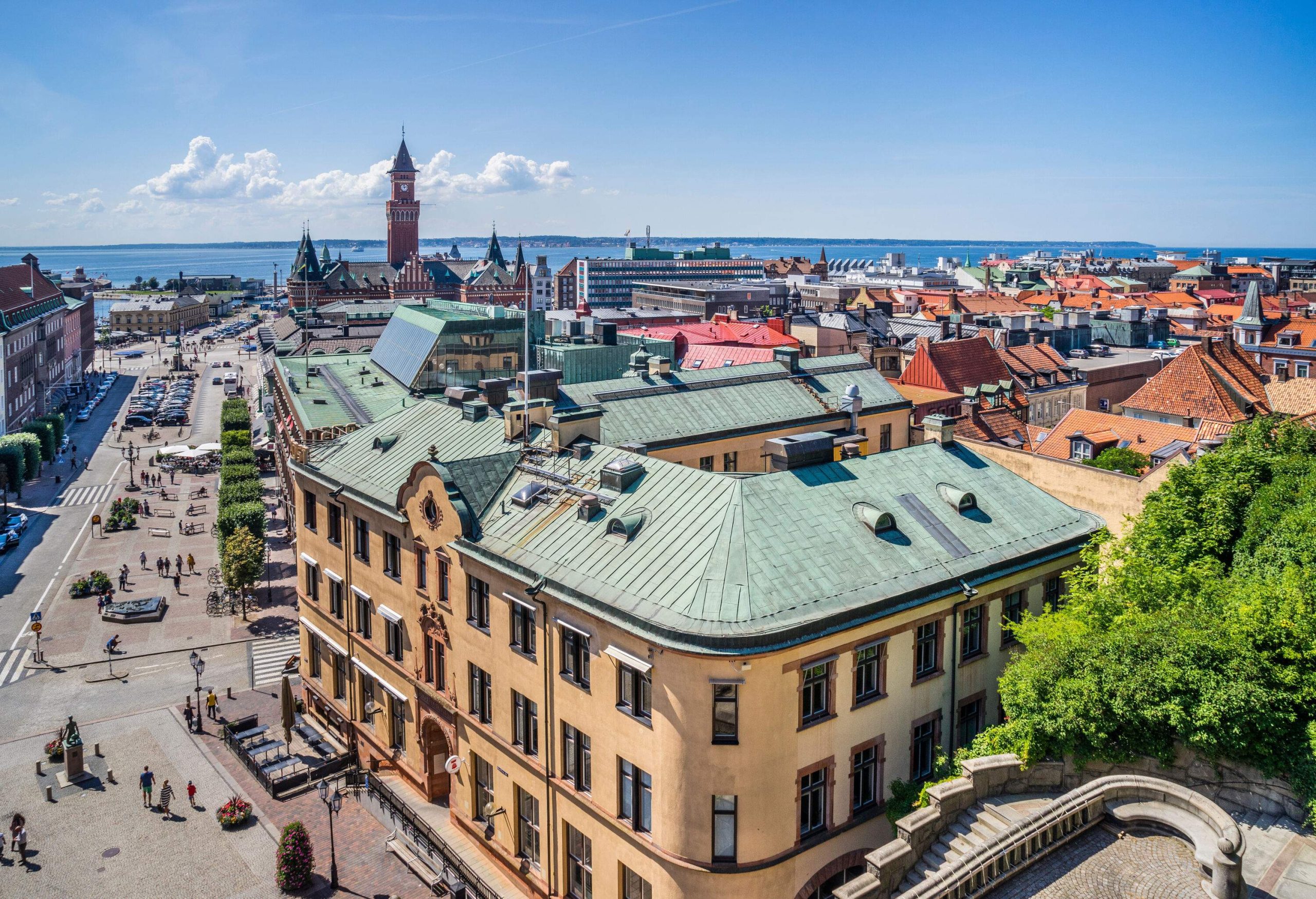 Rooftops of a city with a clock tower and a distant ocean.