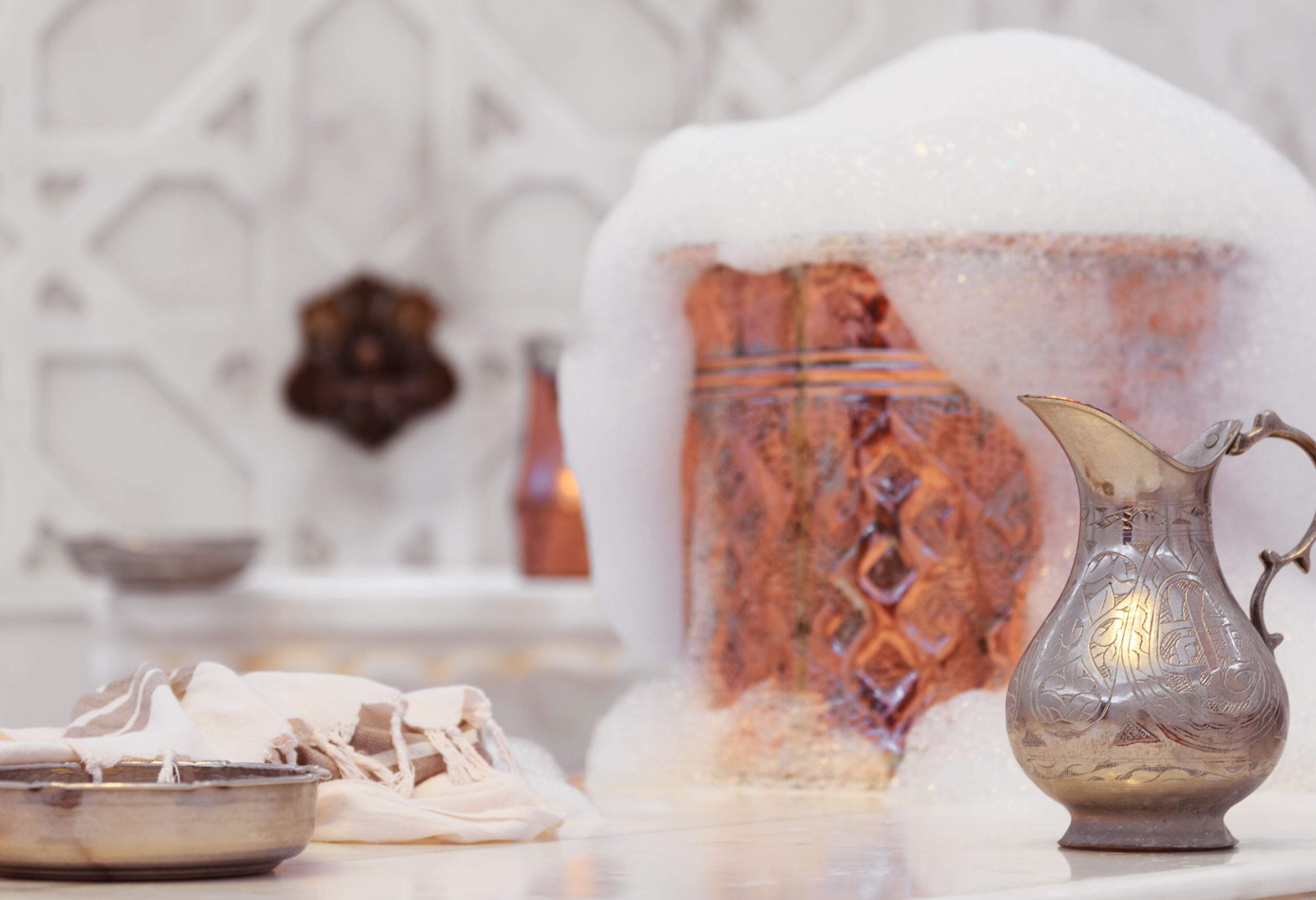 A classic steel water jar and overflowing foam in a copper bowl on a table.