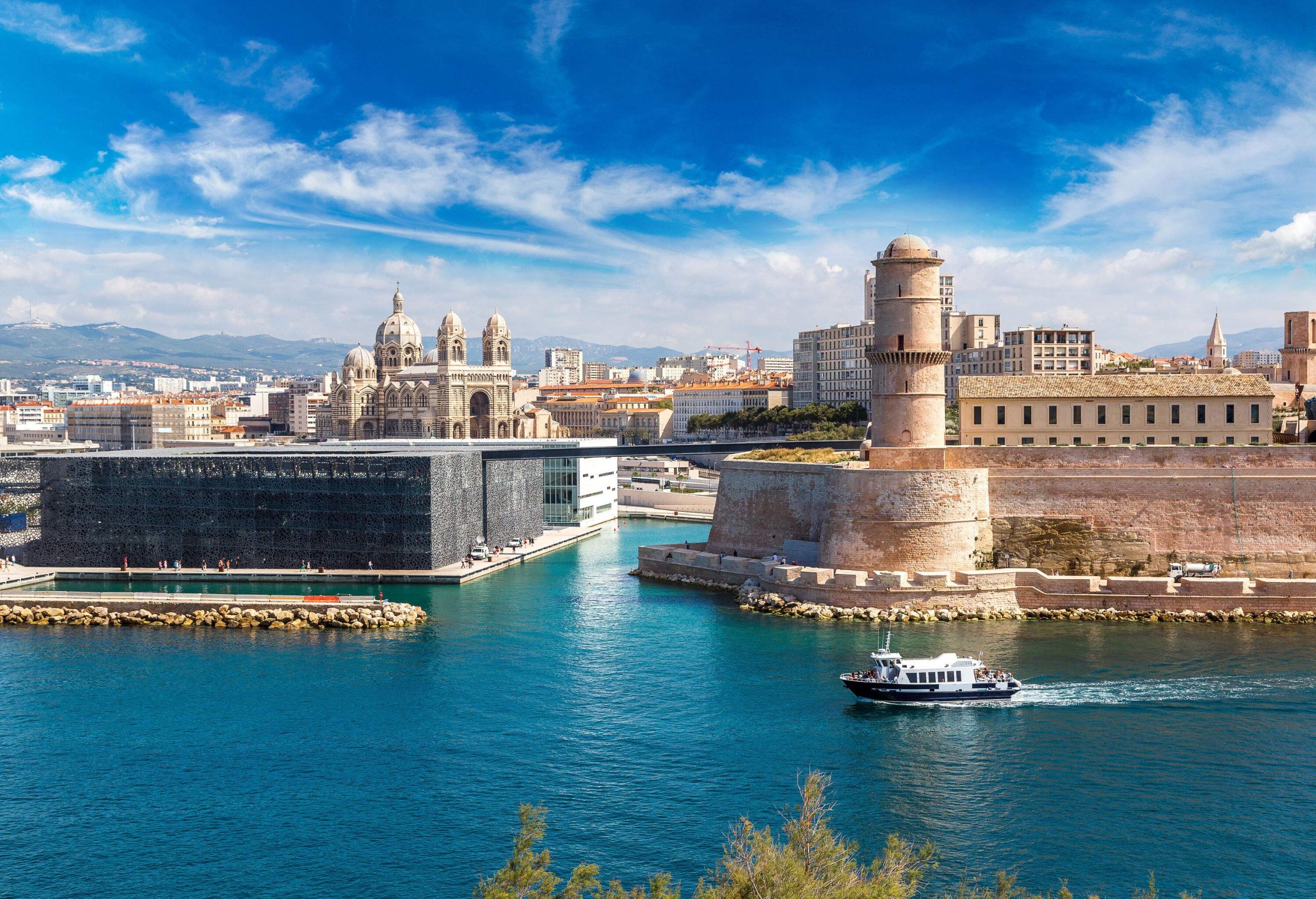 A boat cruises on a small bay along a waterfront tower and a museum with latticed exteriors.