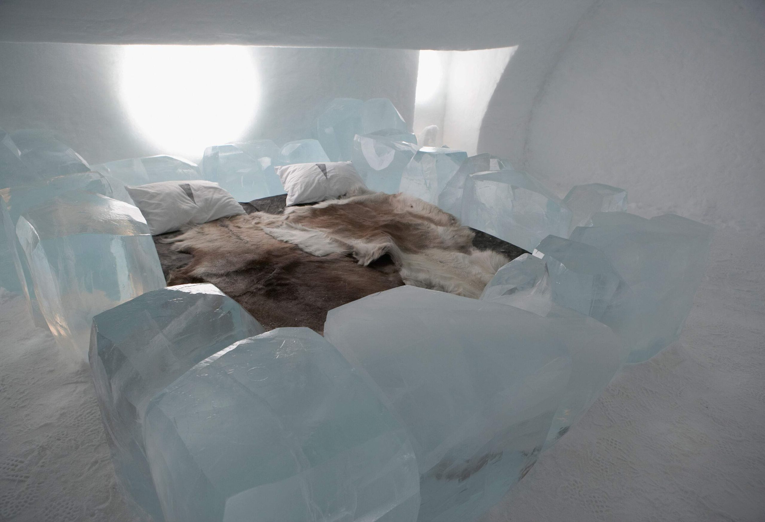 A bedroom set in ice, complete with a bed and chunks of ice all around it.