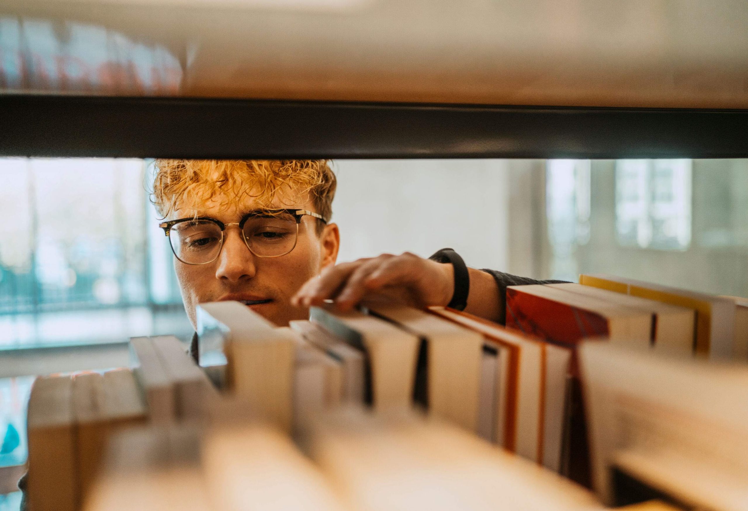 A blonde man browsing through books on the shelf.