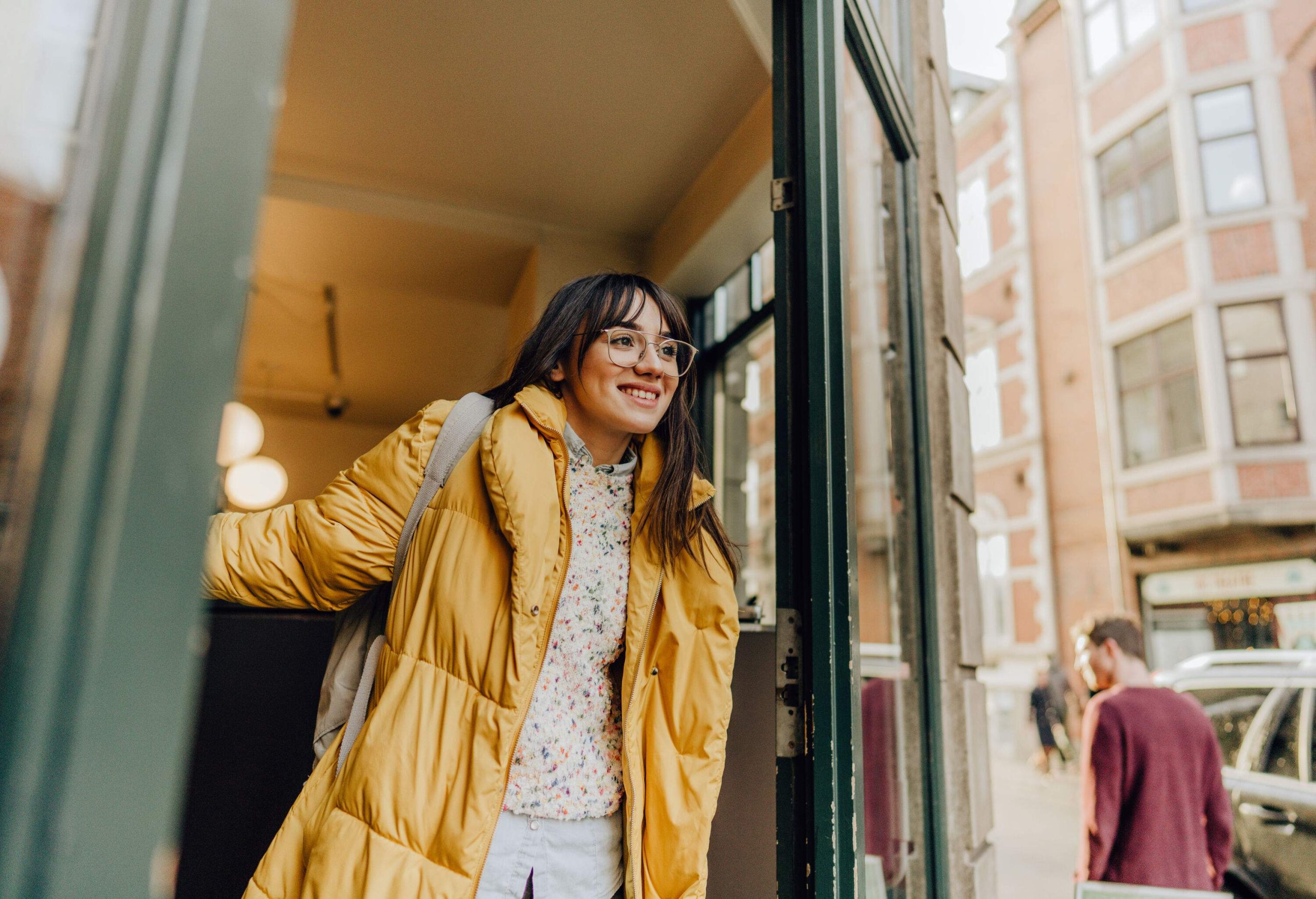 A woman in a yellow puffer jacket smiles as she leaves a shop.