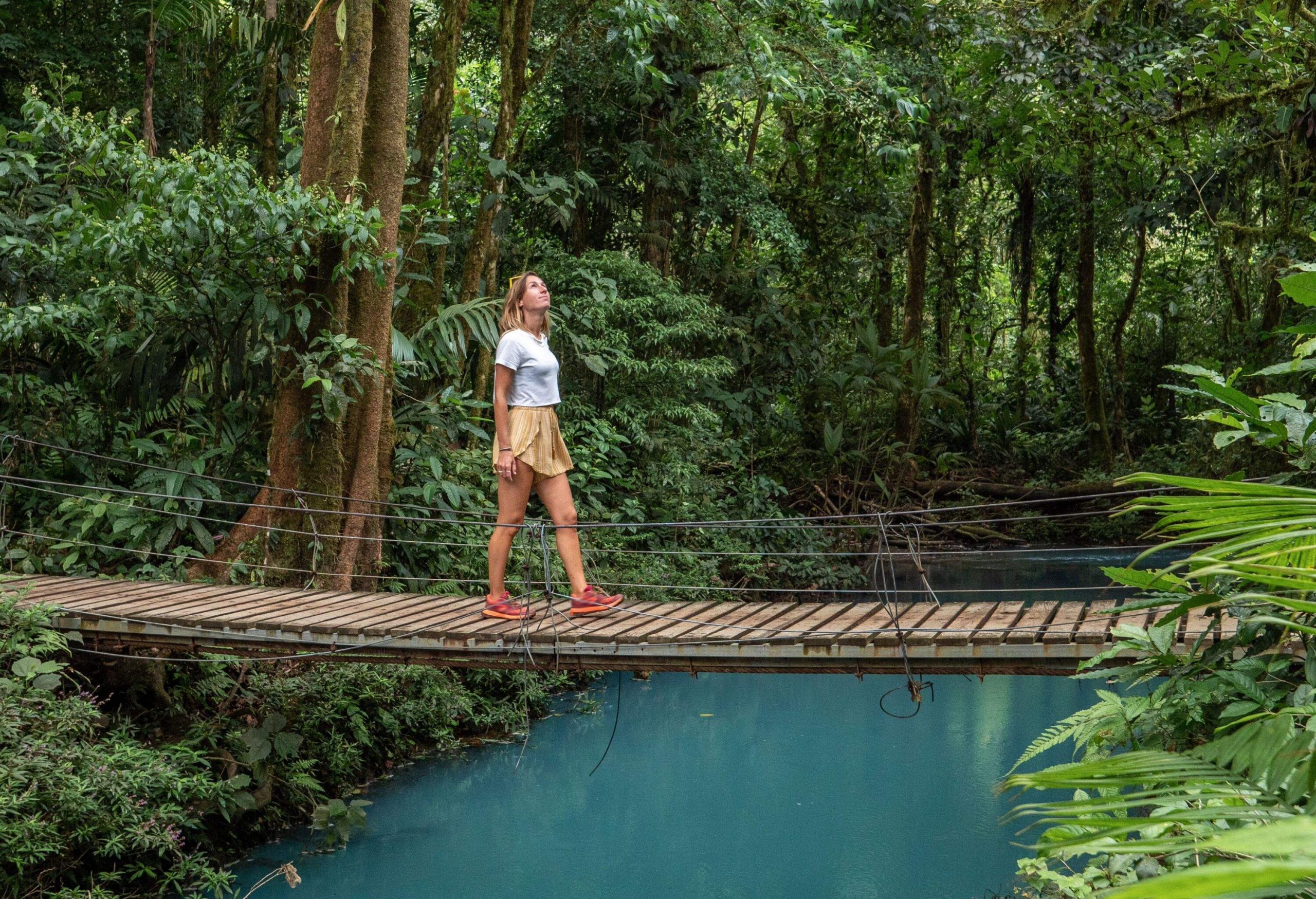 Young woman wandering in tropical rainforest walking on bridge over turquoise lagoon, Costa Rica