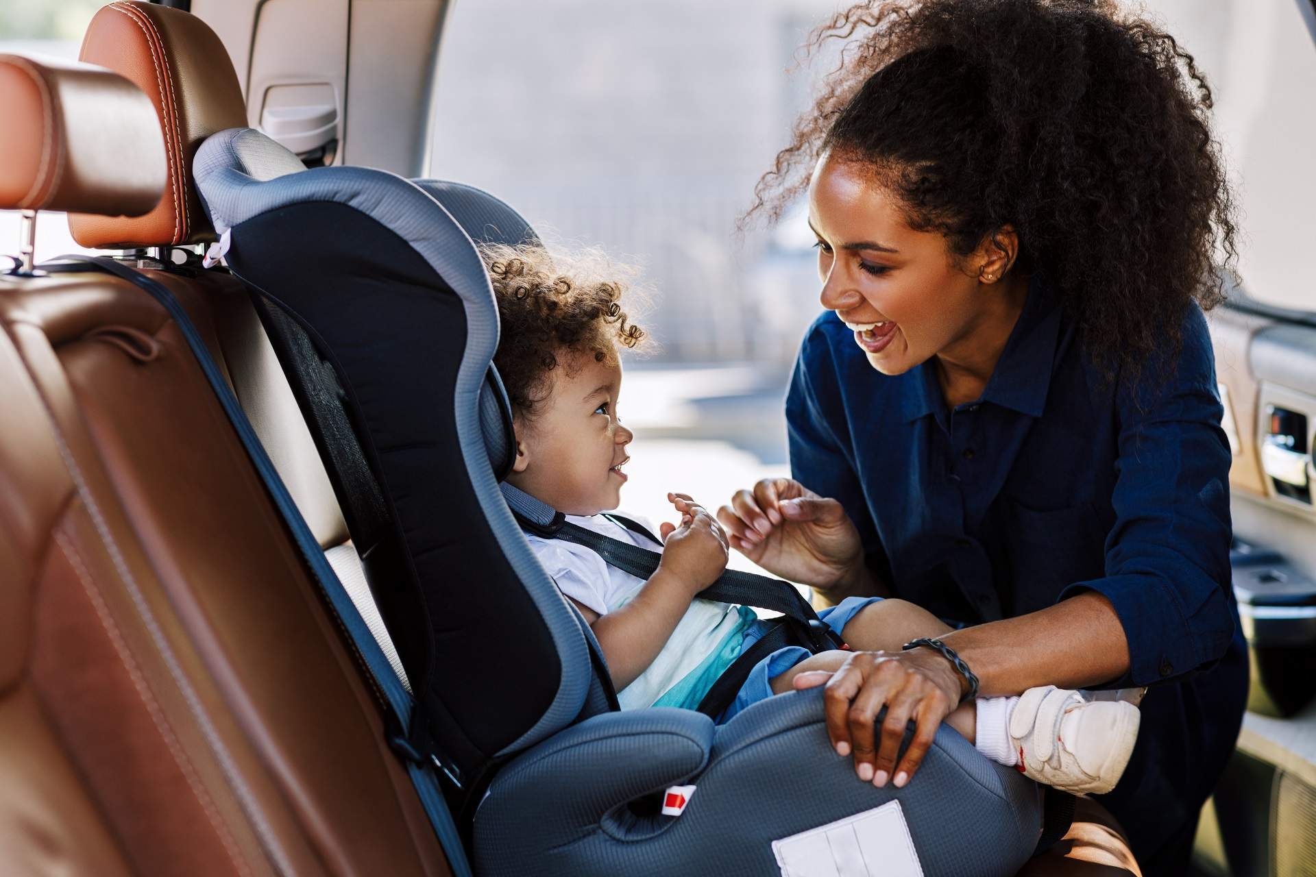 Happy mother looking at her son in a baby seat. Young female preparing kid for a trip. THEME_PERSON_PARENT_CHILD_CAR_CAR-SEAT-GettyImages-1189927309