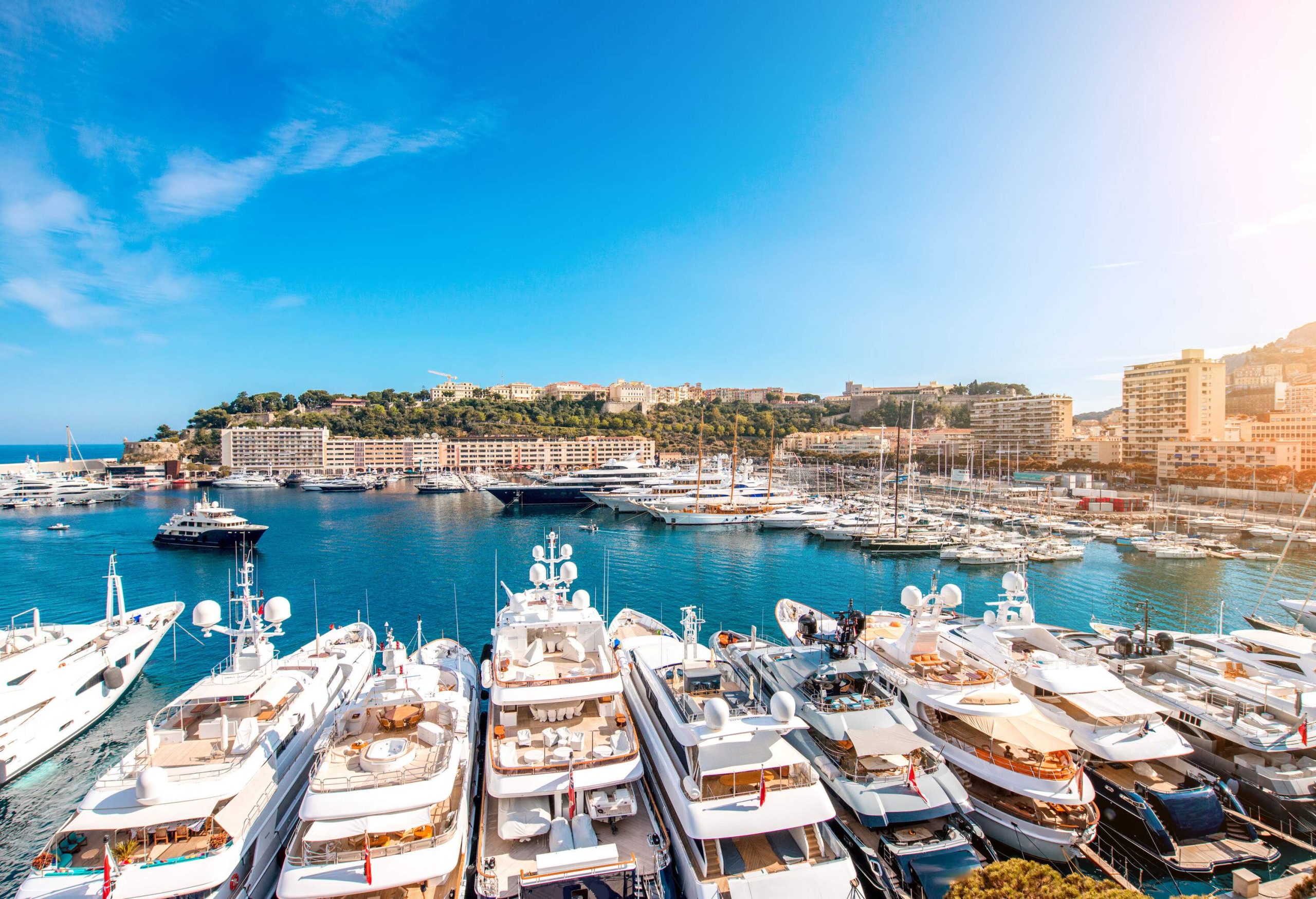 Luxury yachts glisten in the marina, while elegant buildings form a backdrop along the coast.