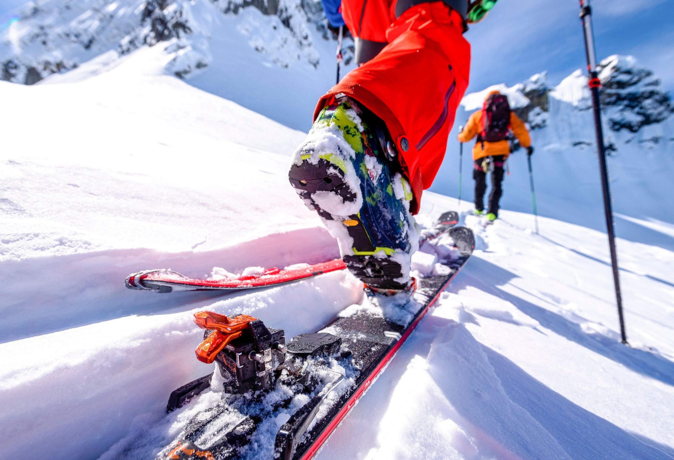 Details of a skier gliding down a slope with snow sticking all over the blades and shoes.