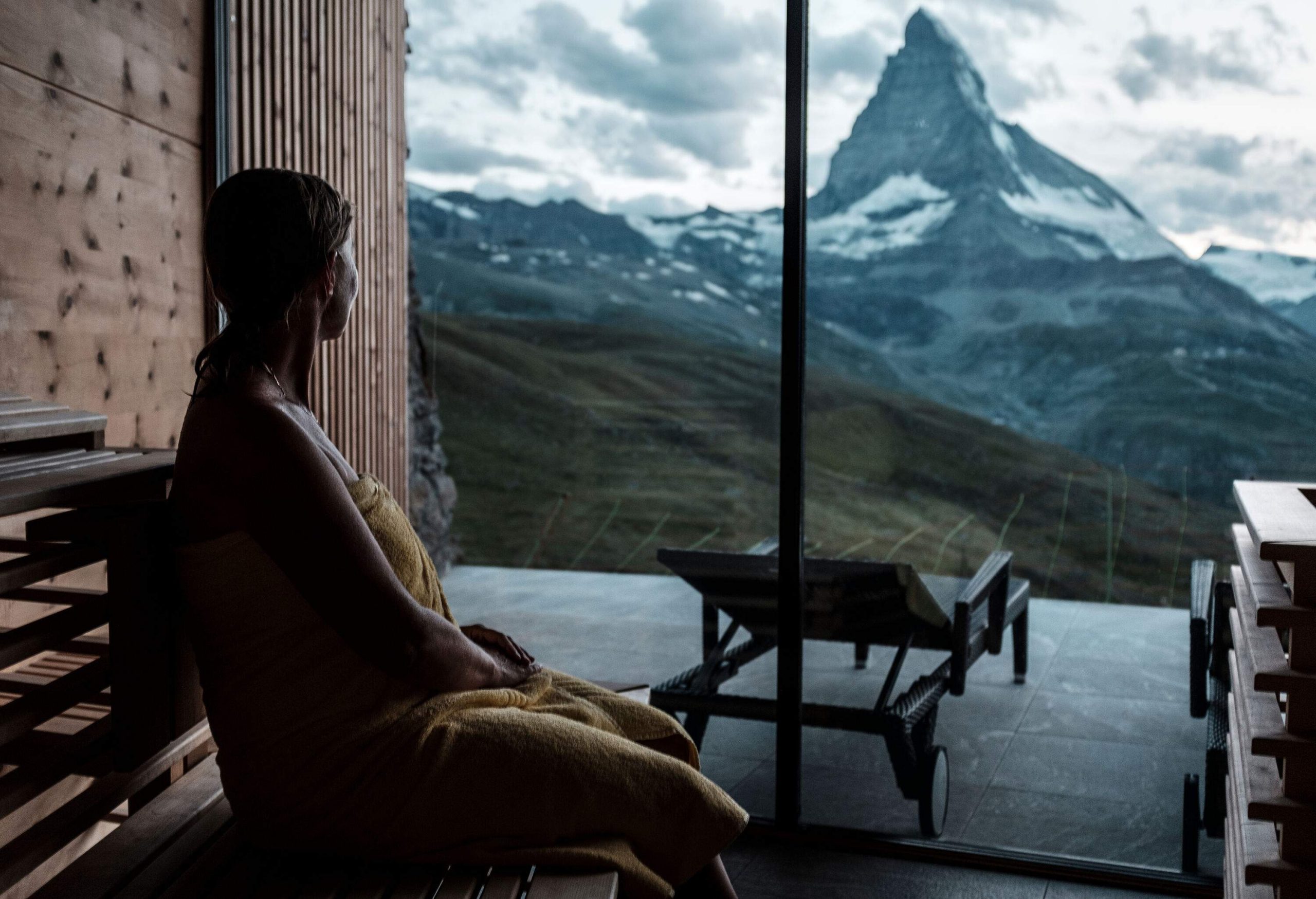 A silhouette shows a solitary person sitting on a wooden bench, lost in contemplation as they take in the rough and rugged landscape stretching out before them.