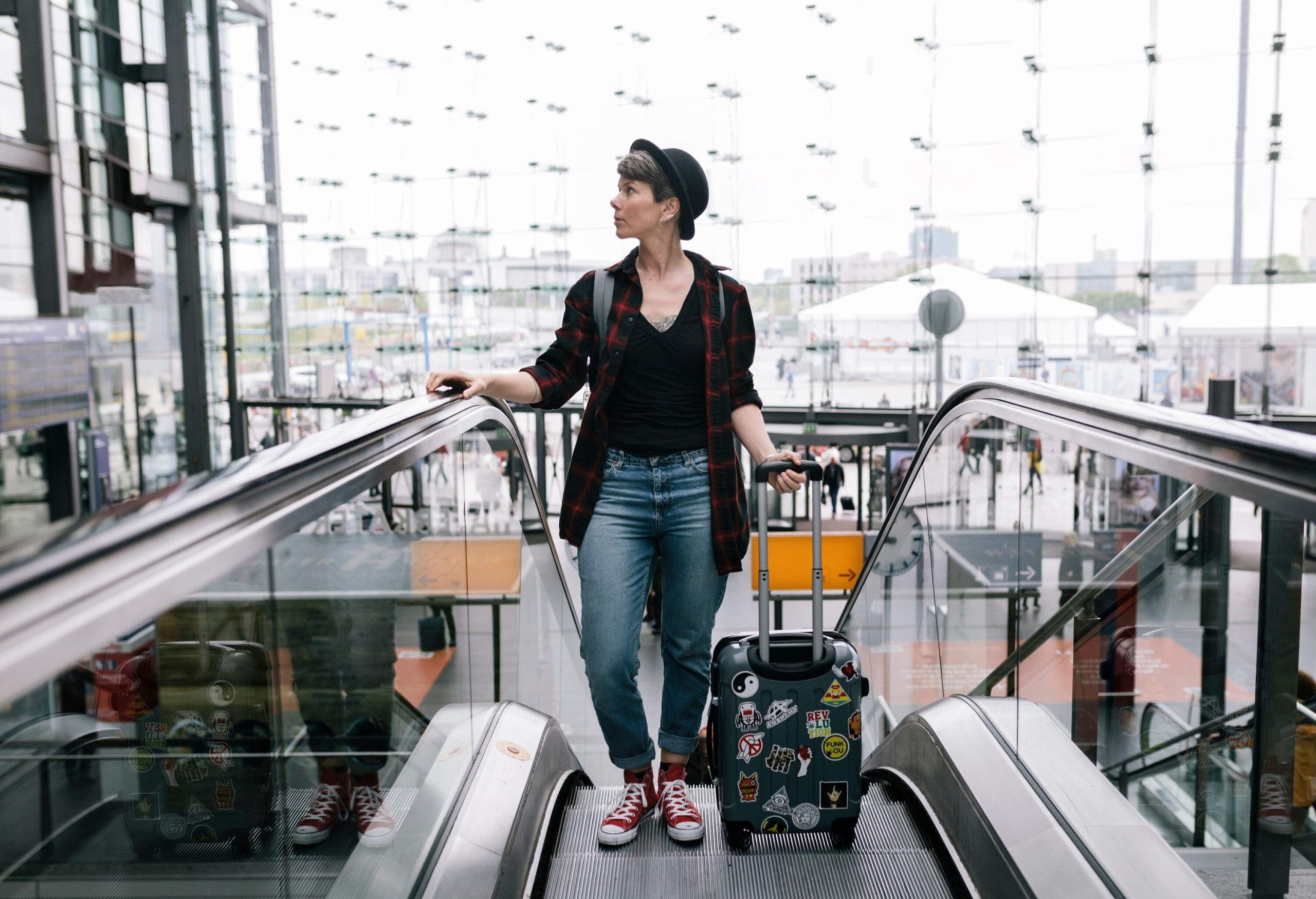 A woman with a suitcase riding an escalator.