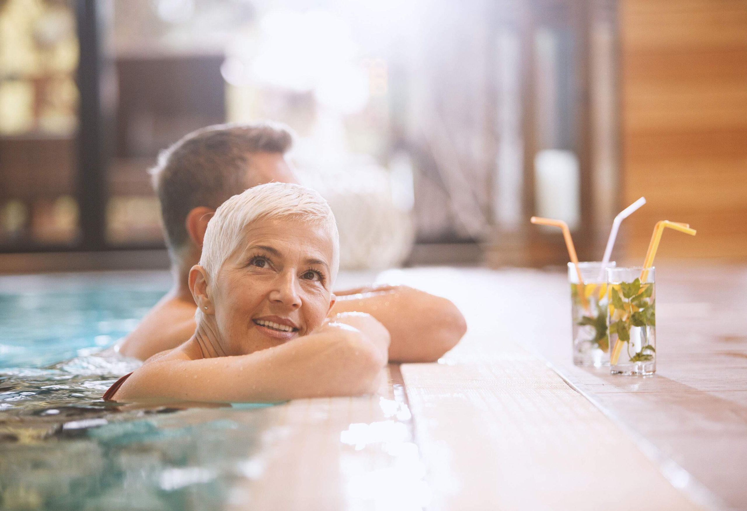 A couple having a glass of drinks while soaking in an indoor swimming pool spa.