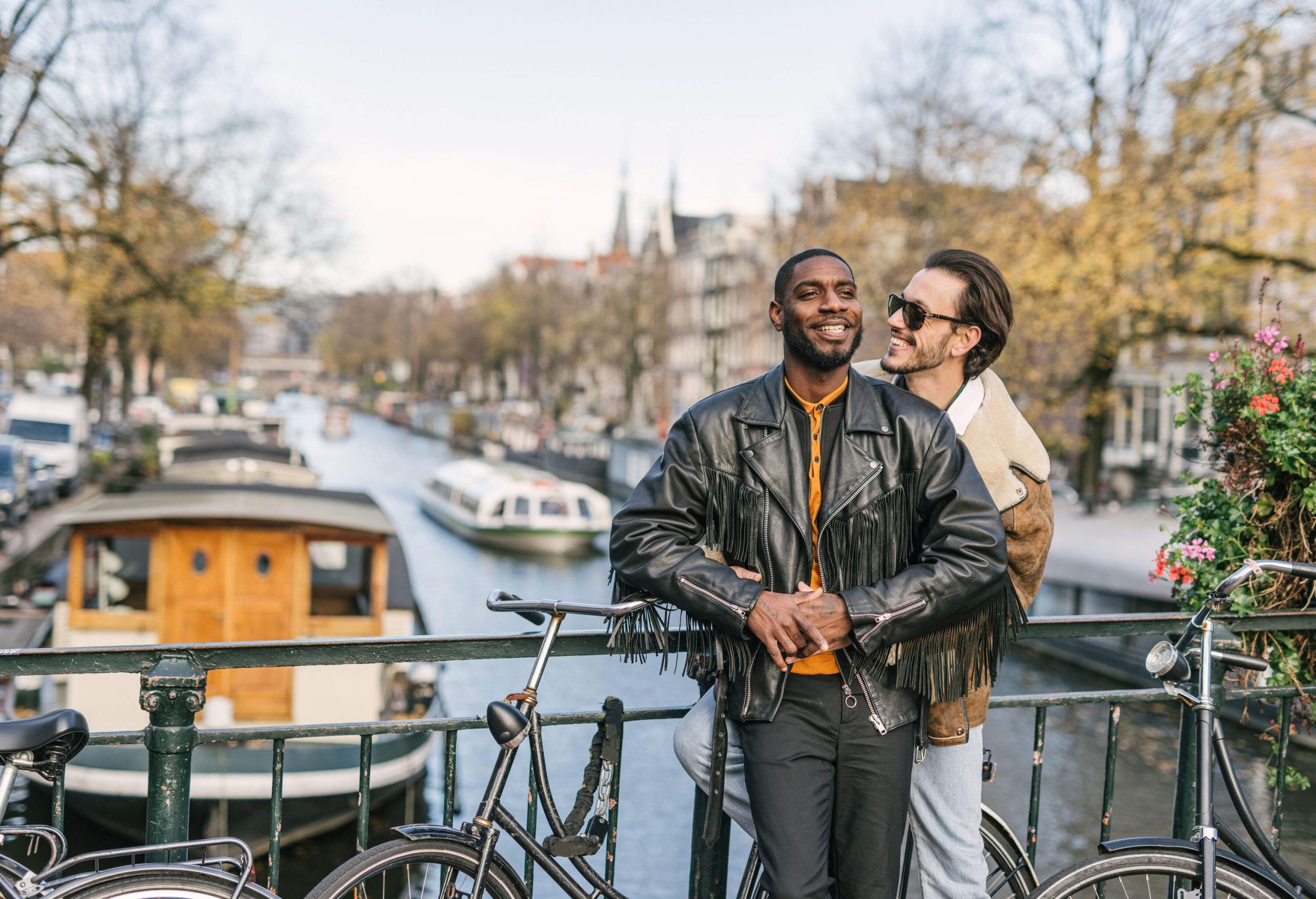 A contented couple leans on the guardrail of a picturesque bridge, overlooking a serene canal, as they enjoy each other's company amidst parked bicycles.