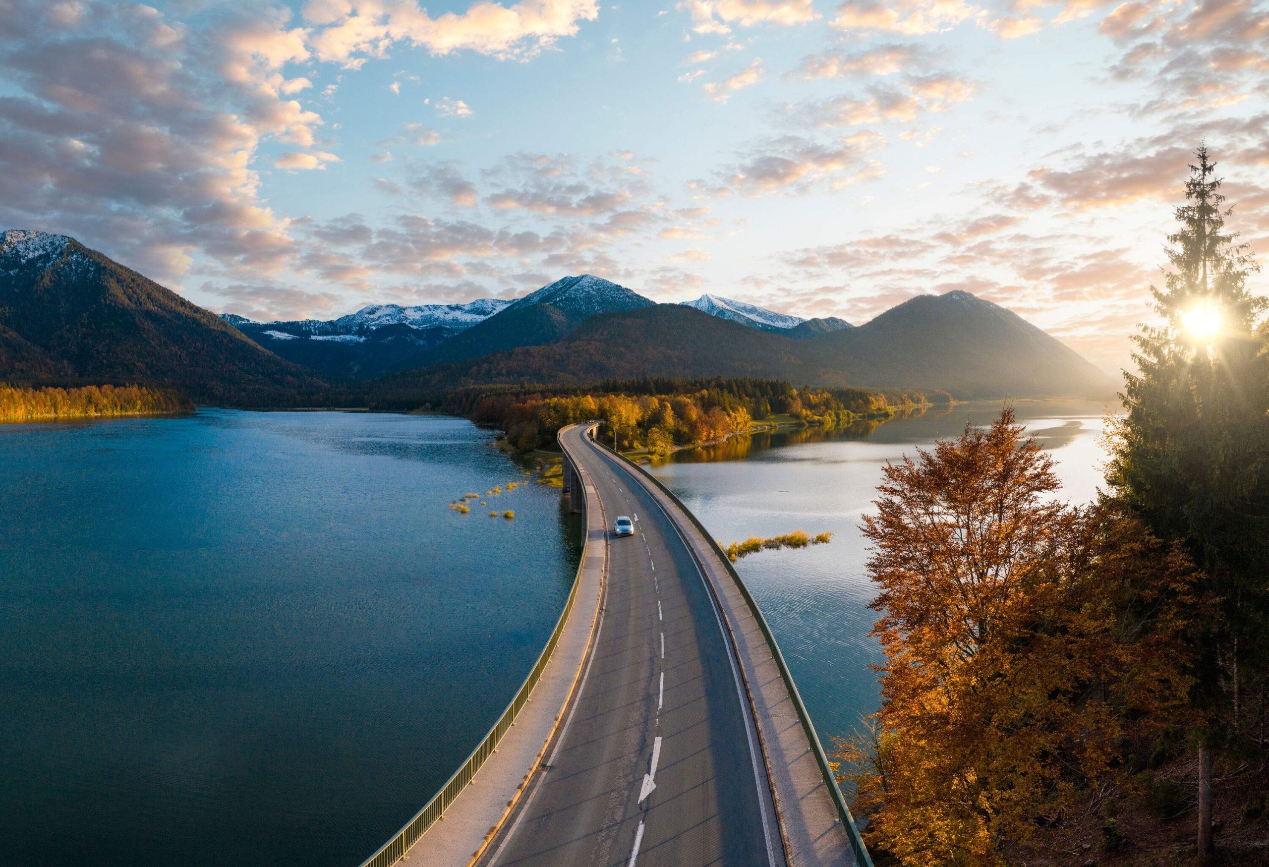 A car travelling on a long road bridge over a lake.