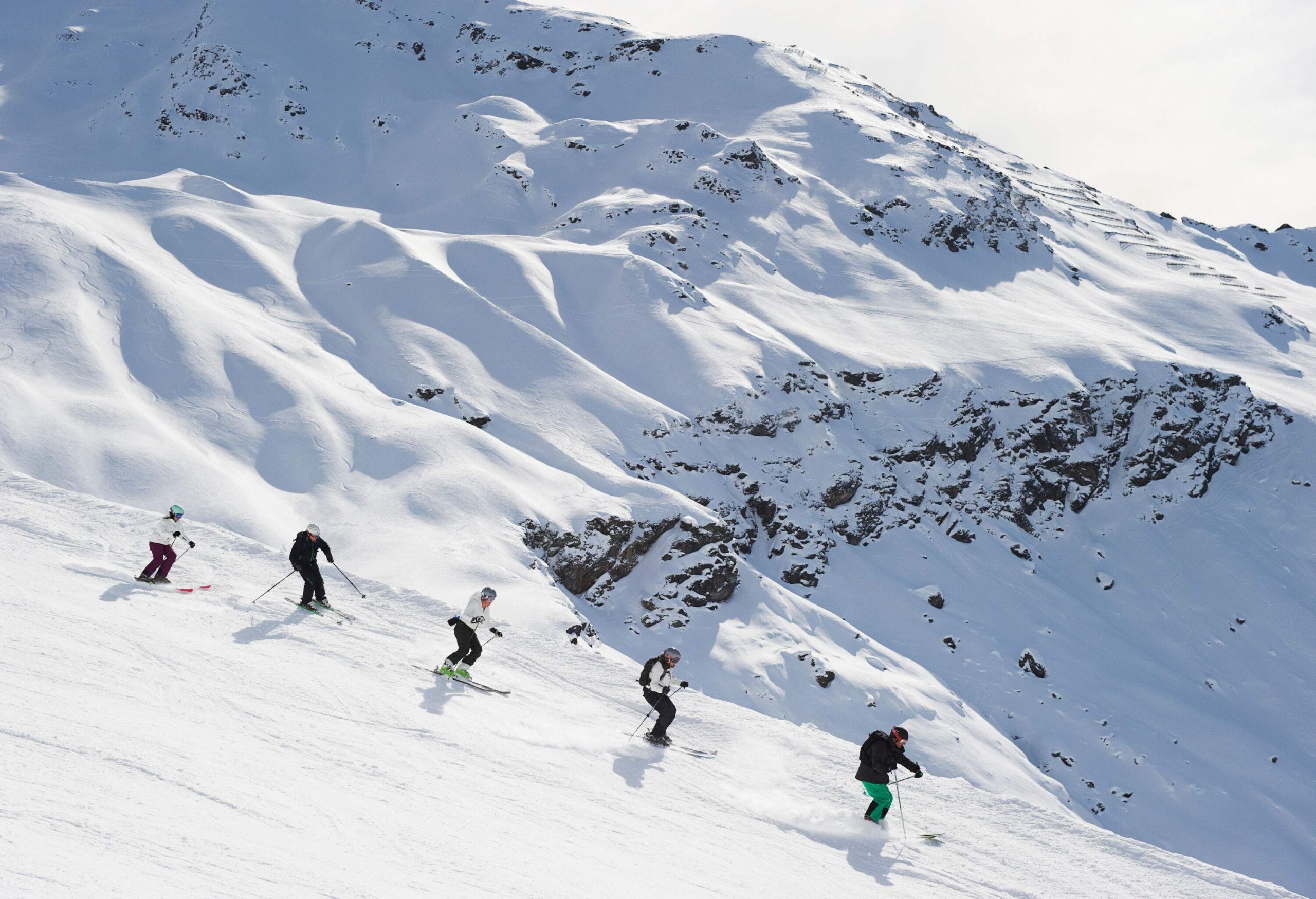 Skiers descending on the powder snow land of a sloppy ski terrain over looking the mountains covered in snow.