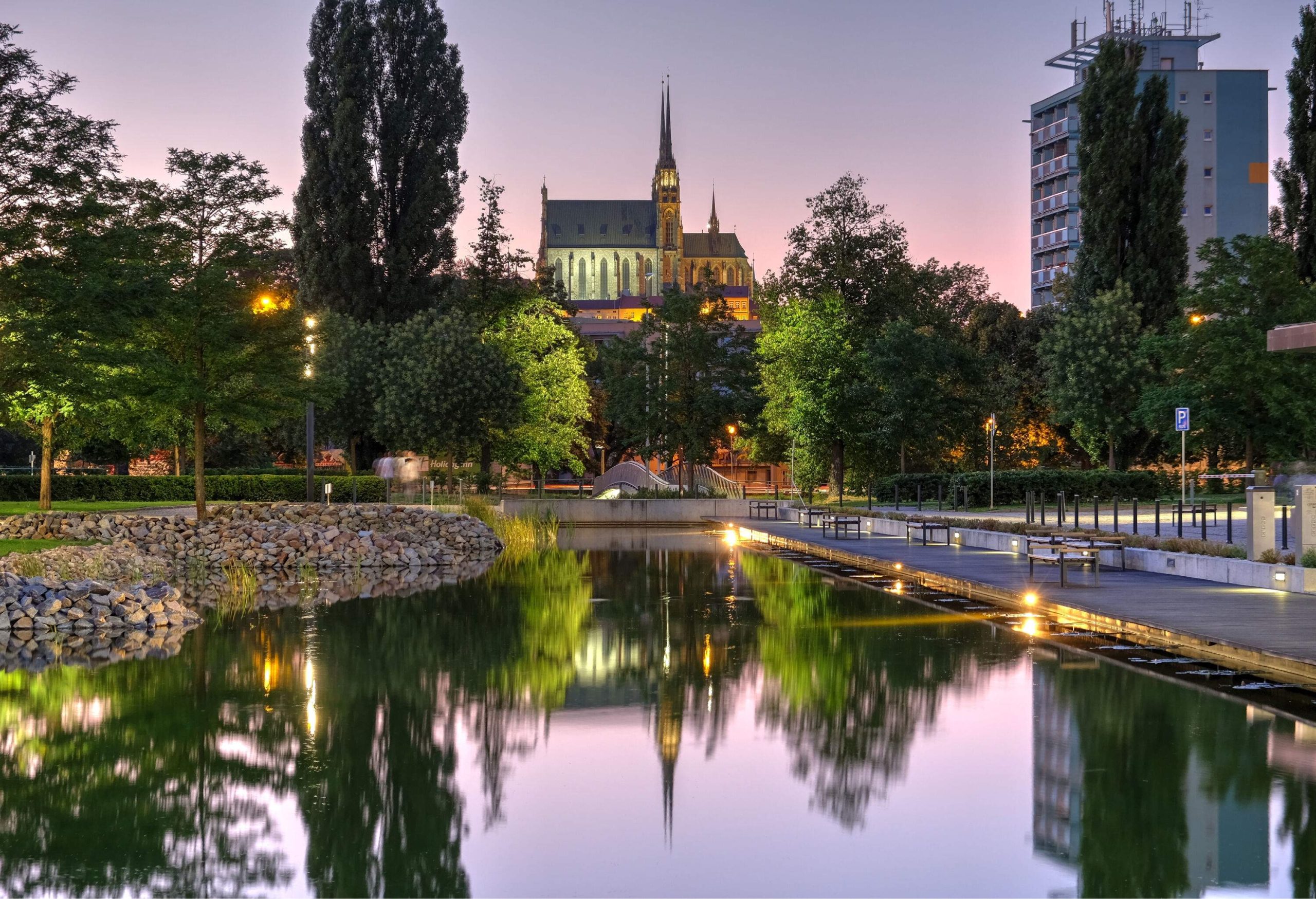 The glassy surface of a pond mirroring its surrounding buildings and trees.