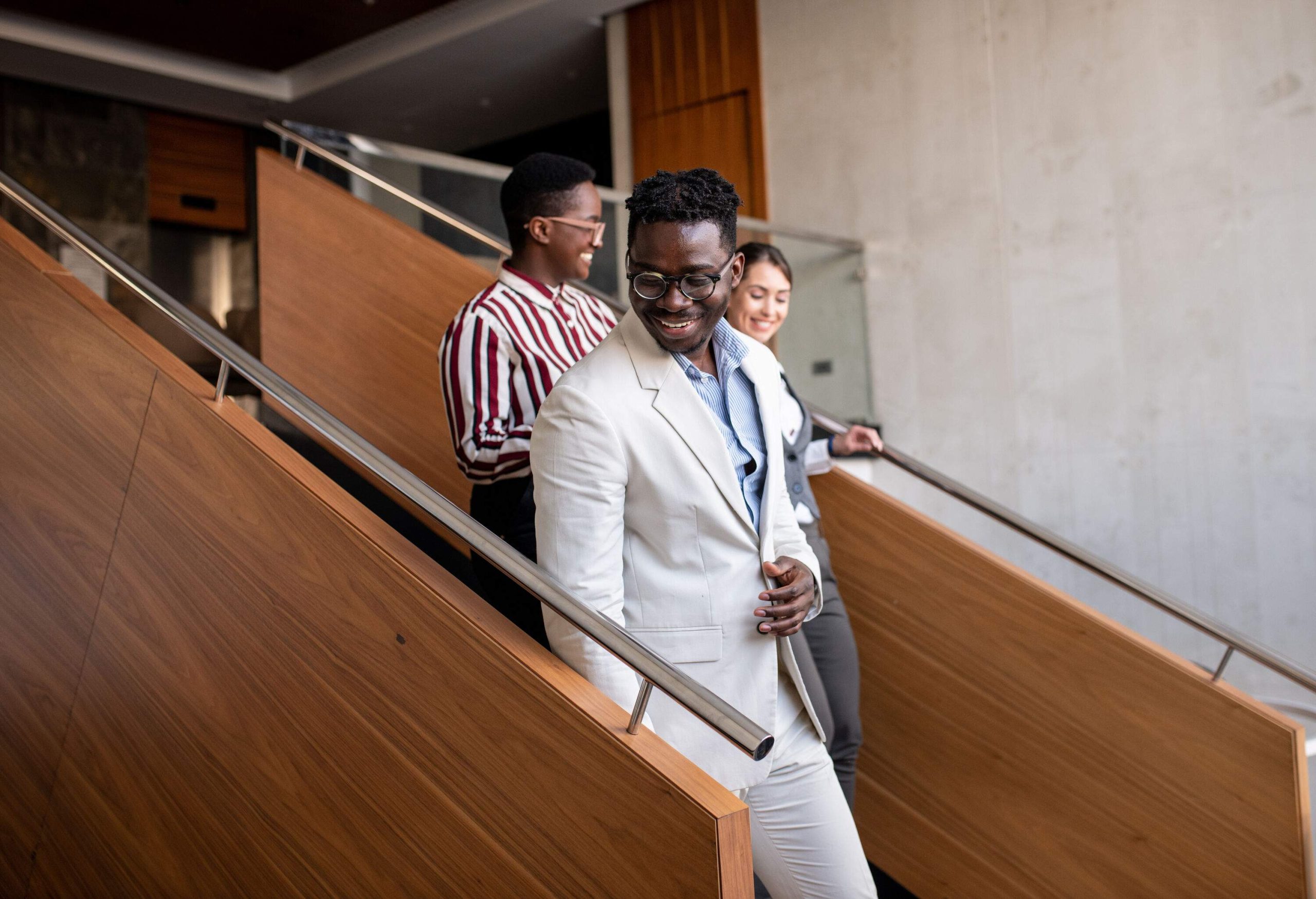 Three young business people walking down the staircase in a hotel. Three young interracial coworkers walking together on the staircase in a hotel. Group of young mixed race colleagues on a casual meeting. Interracial group of businesspeople.