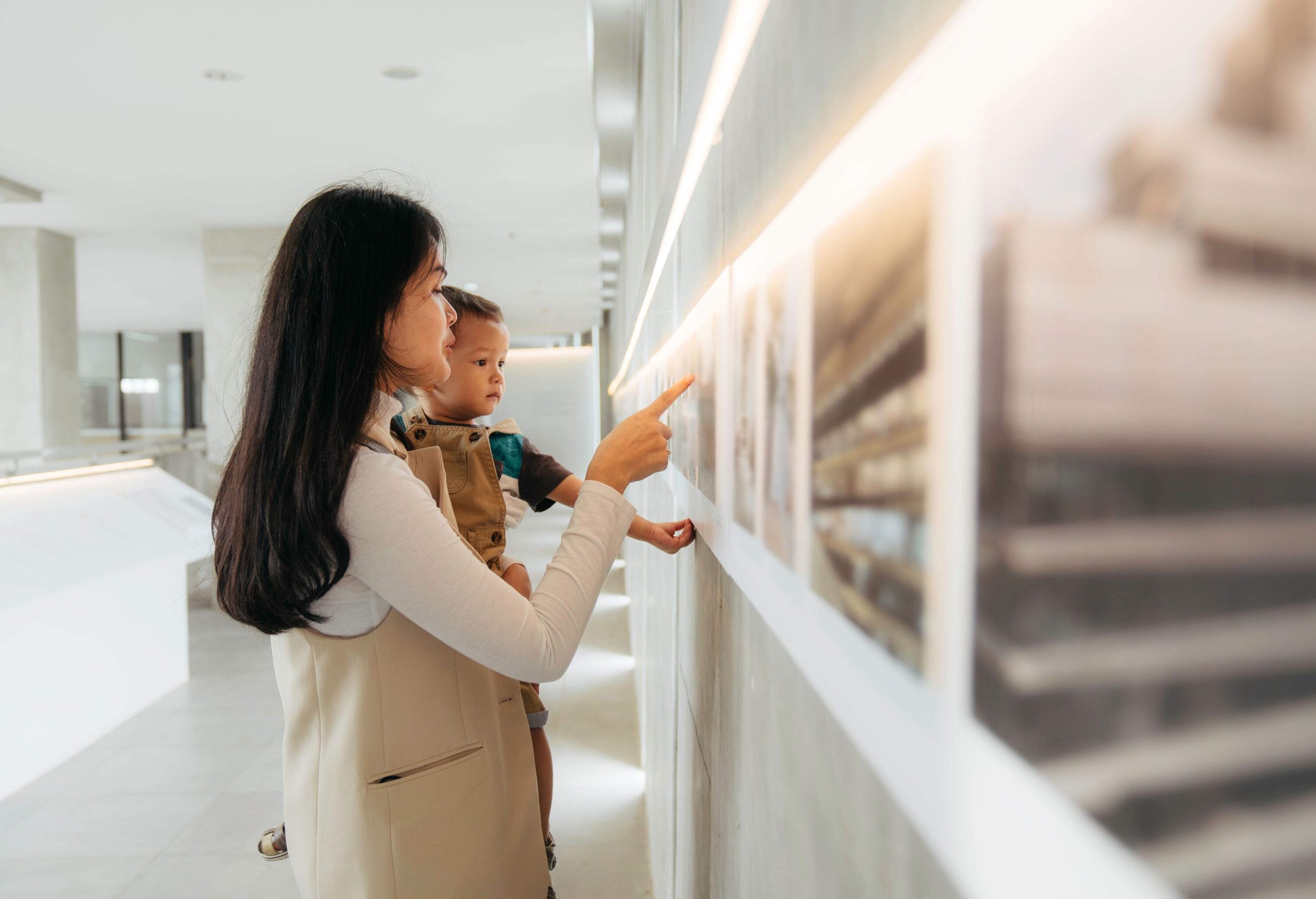 A woman holding a small child as she points to a painting on the wall.