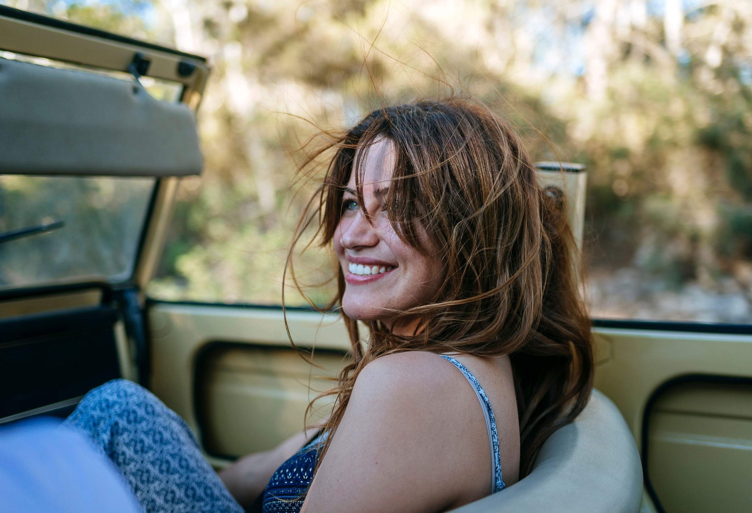 A smiling woman sitting in a convertible car with open roof.