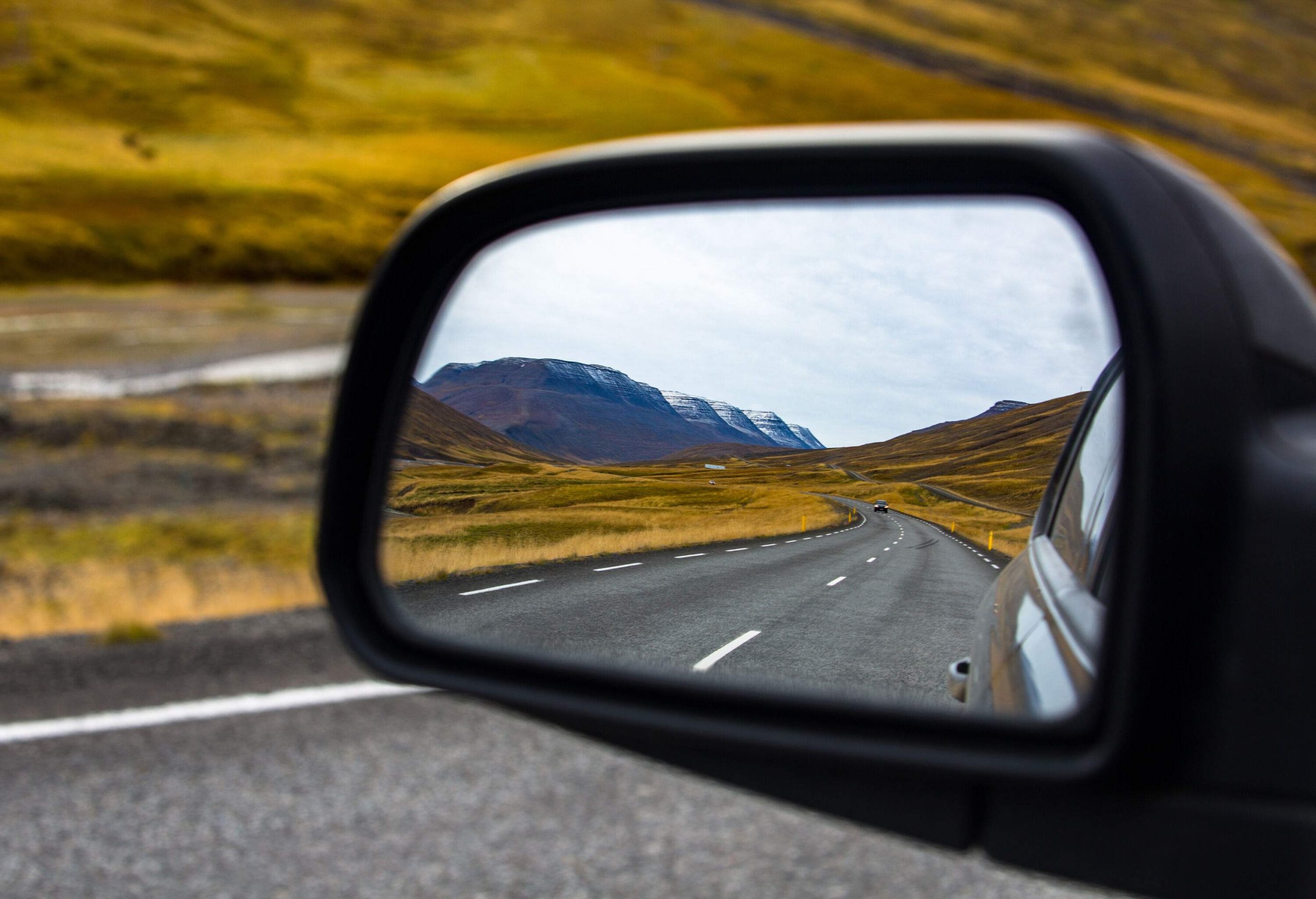A car's side mirror with a reflection of an empty highway across a grass field.