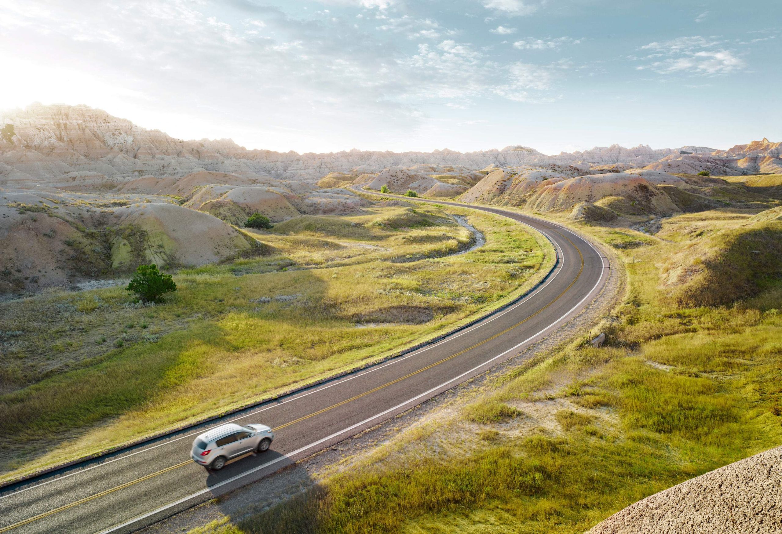 A silver car travels on a road across a hilly landscape.