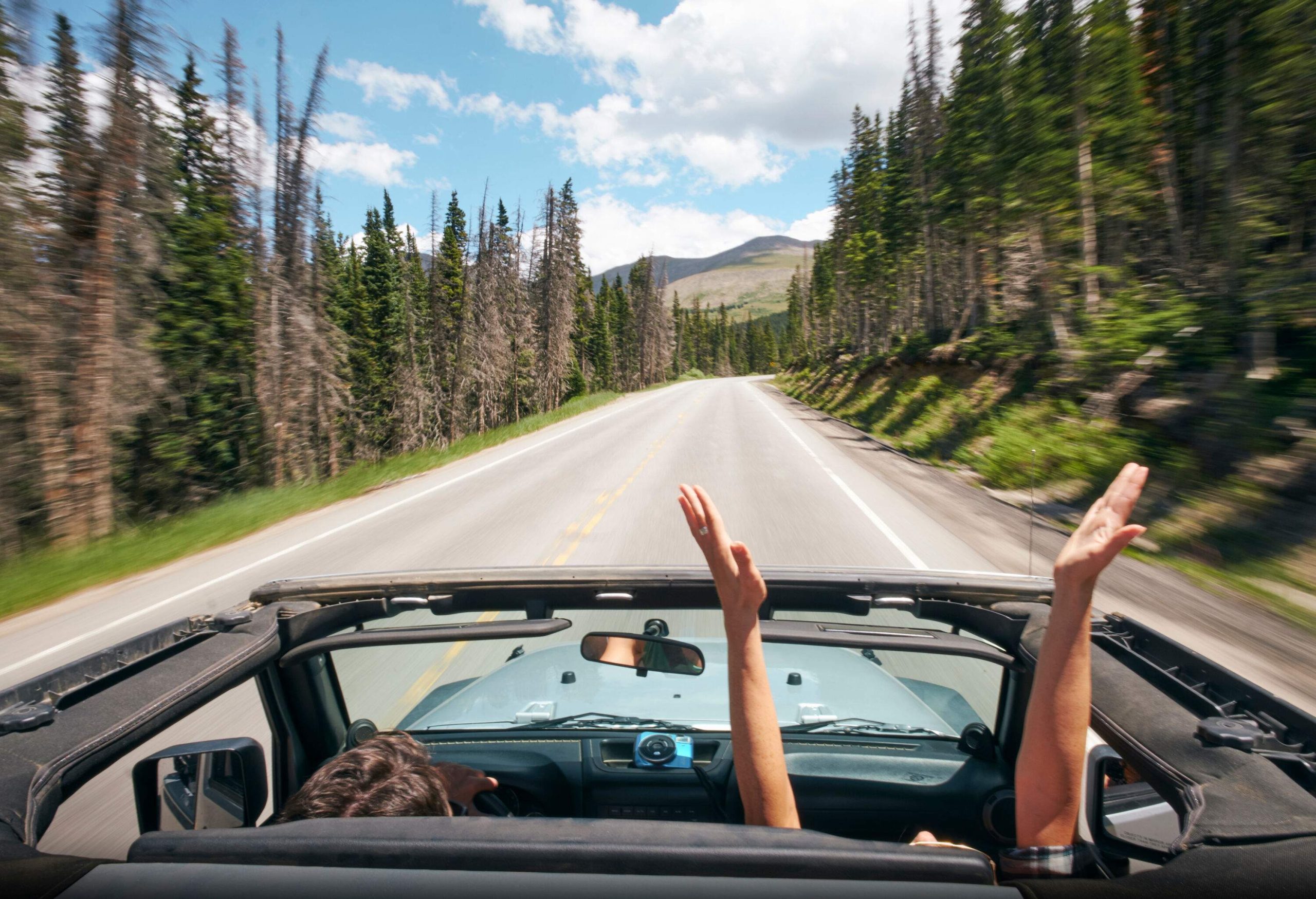 A man in the passenger seat stretching his arms over his head as they drive down the road.