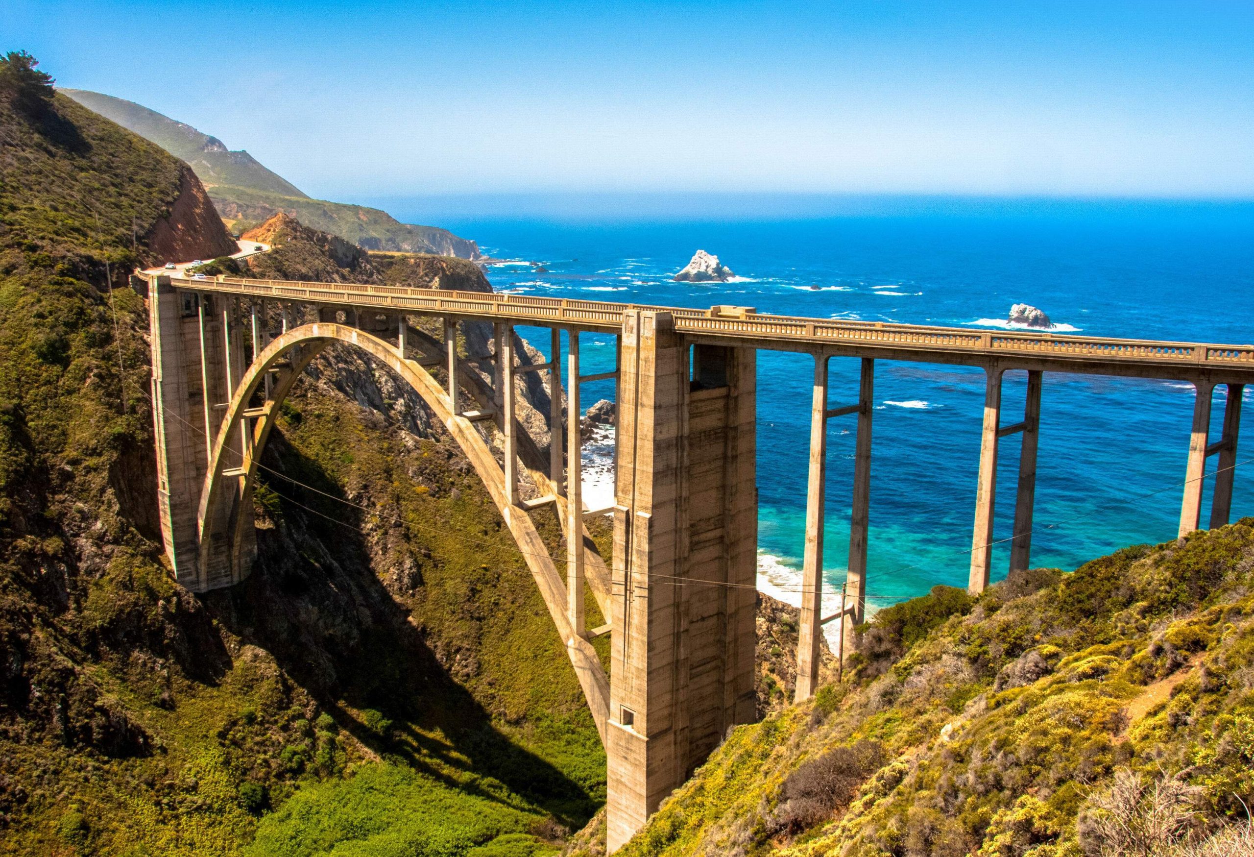 A tall arch bridge across a ravine between two cliffs overlooking the ocean.