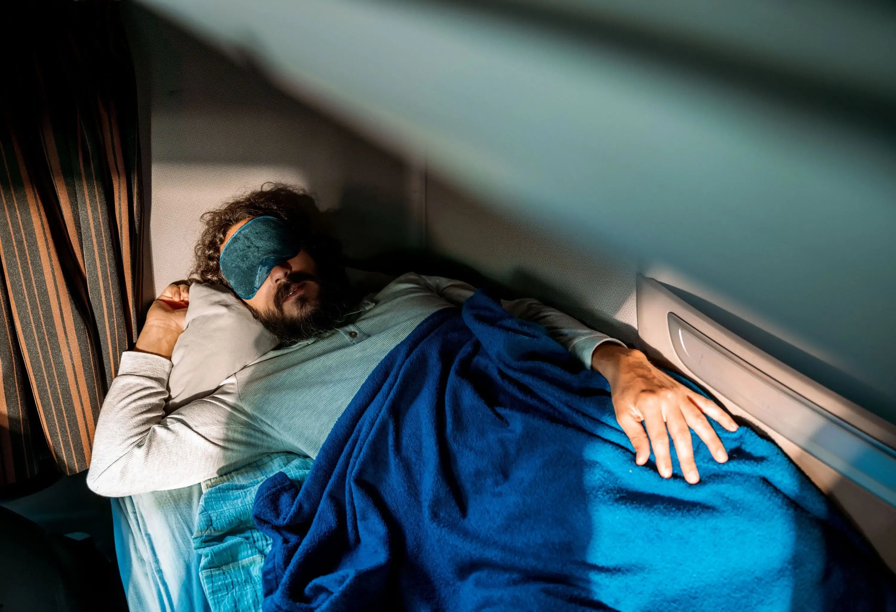 A man wearing an eye mask sleeping in a truck's sleeper cab.