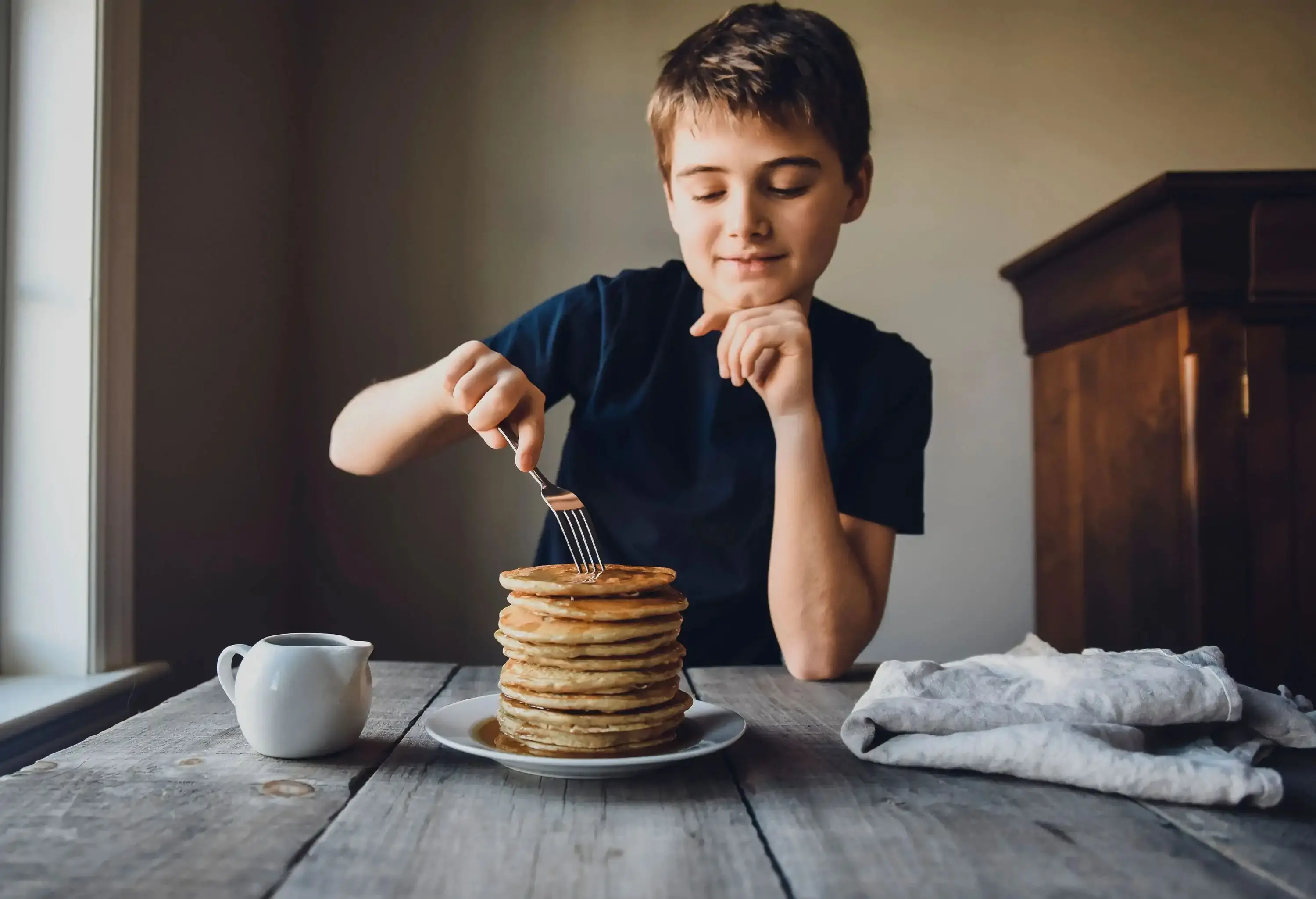 A young boy eating a stack of pancakes drenched in syrup.