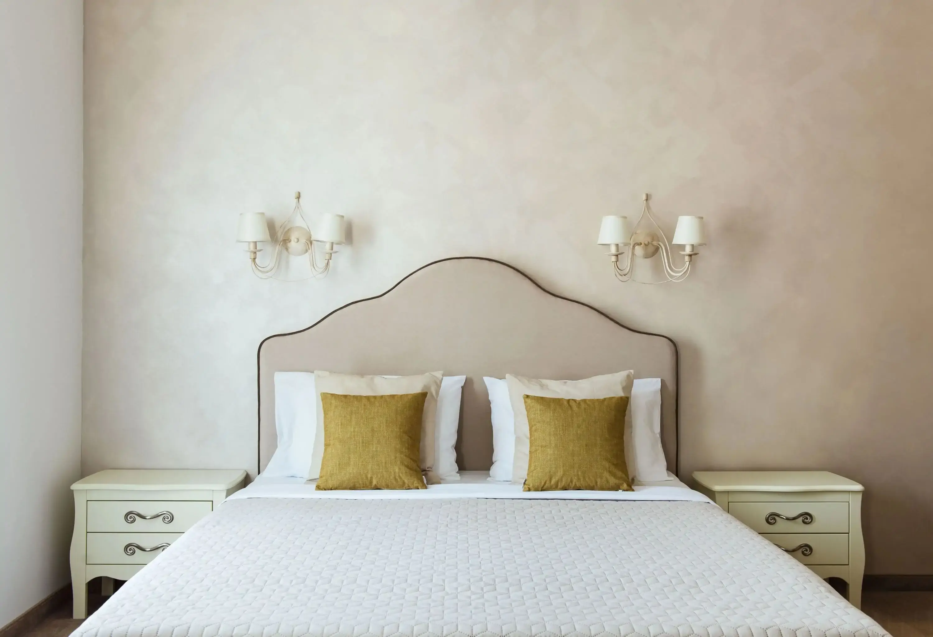 A neatly made bed with wall lamps and end tables on either side.