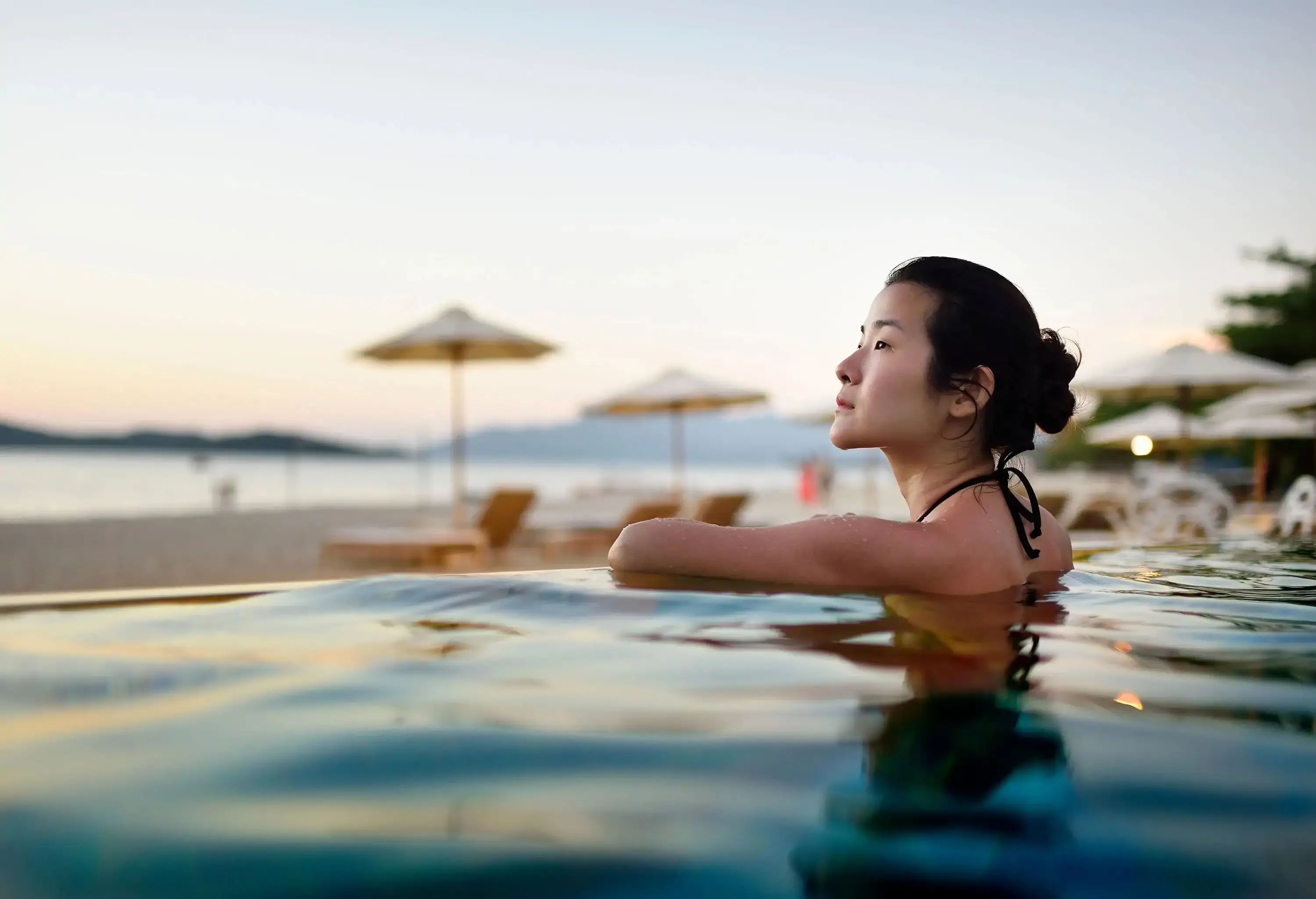 A woman resting on the edge of a swimming pool overlooking the beach.