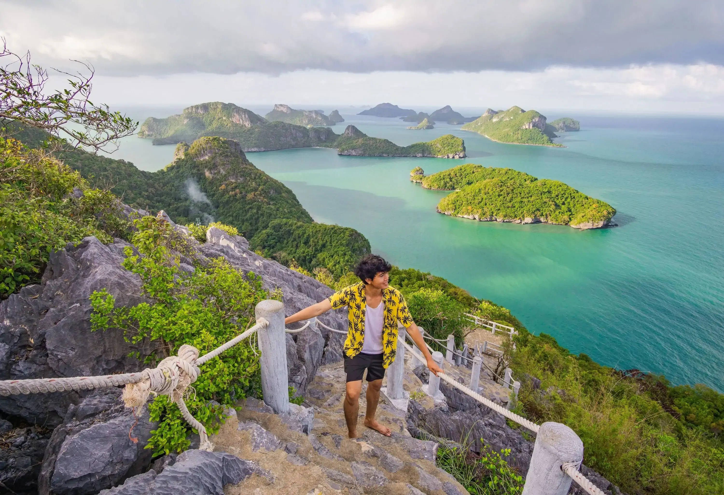 A man stands on a ladder with a view of the mountains below, the emerald sea, Angthong islands, Koh Samui, Suratthani province.