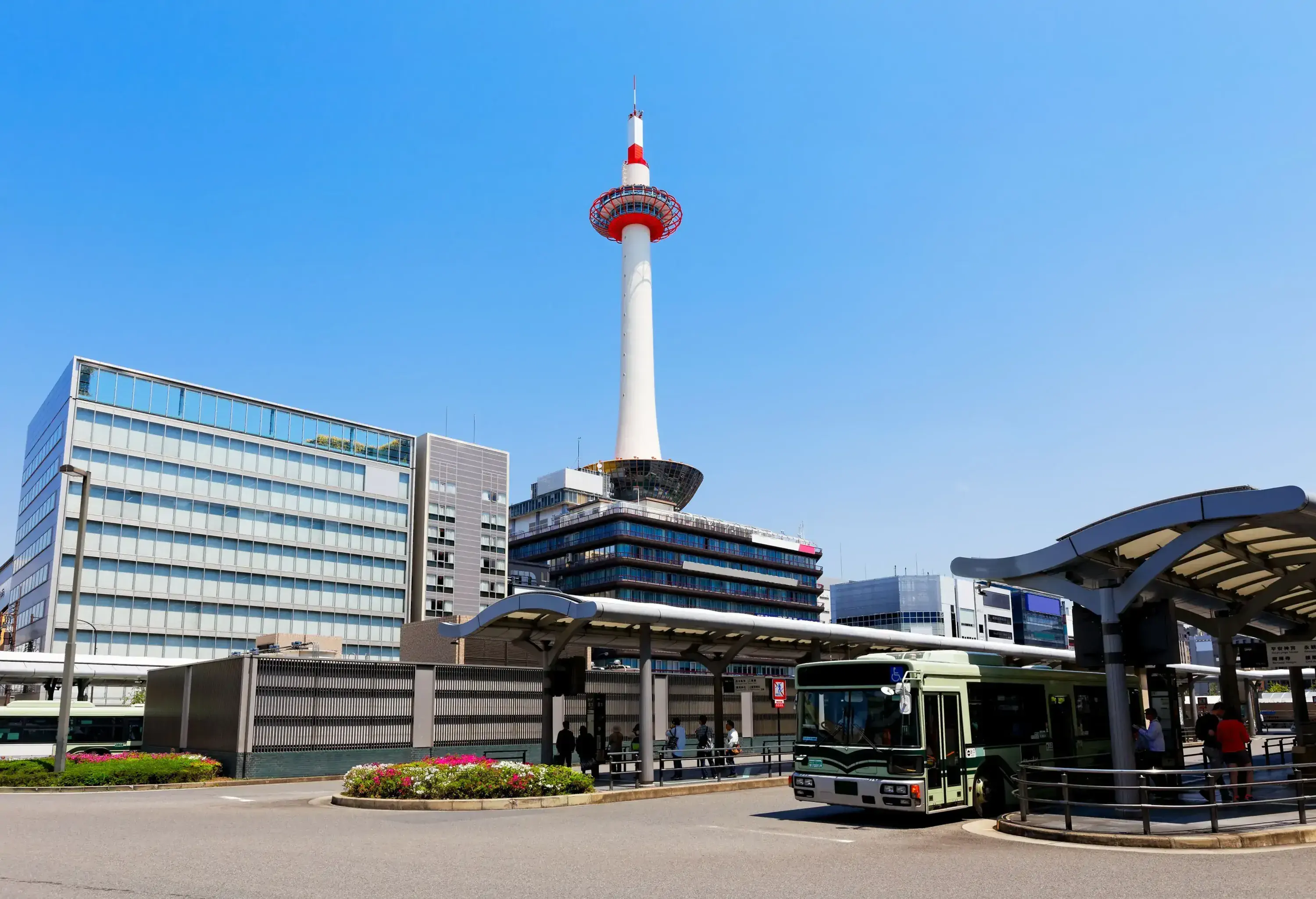 The Kyoto Tower soaring over the surrounding buildings into the clear sky.