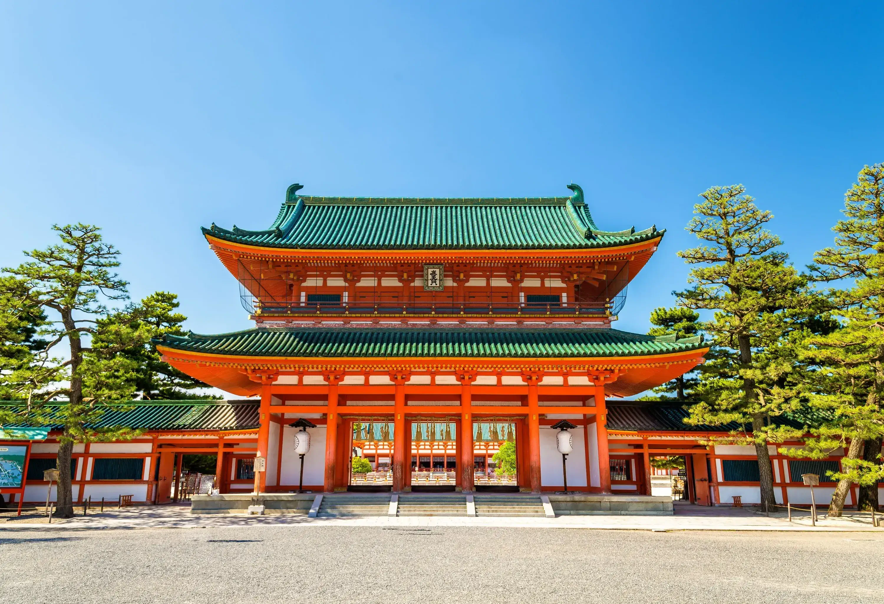 A main gate of a shrine that features orange pillars supporting two tiered roofs with ceramic tiling.