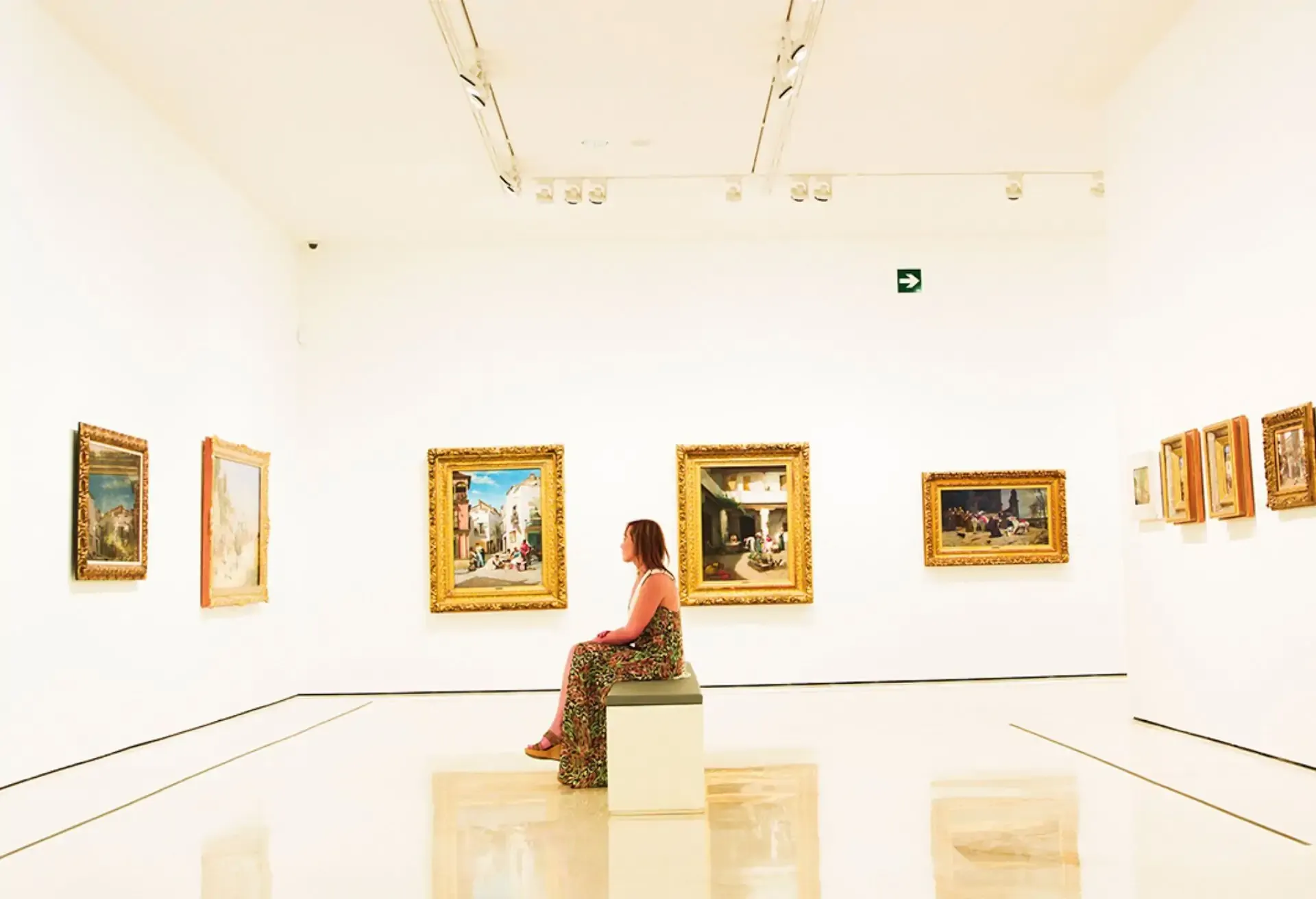 Woman sitting alone admiring classic paintings in a bright art gallery.