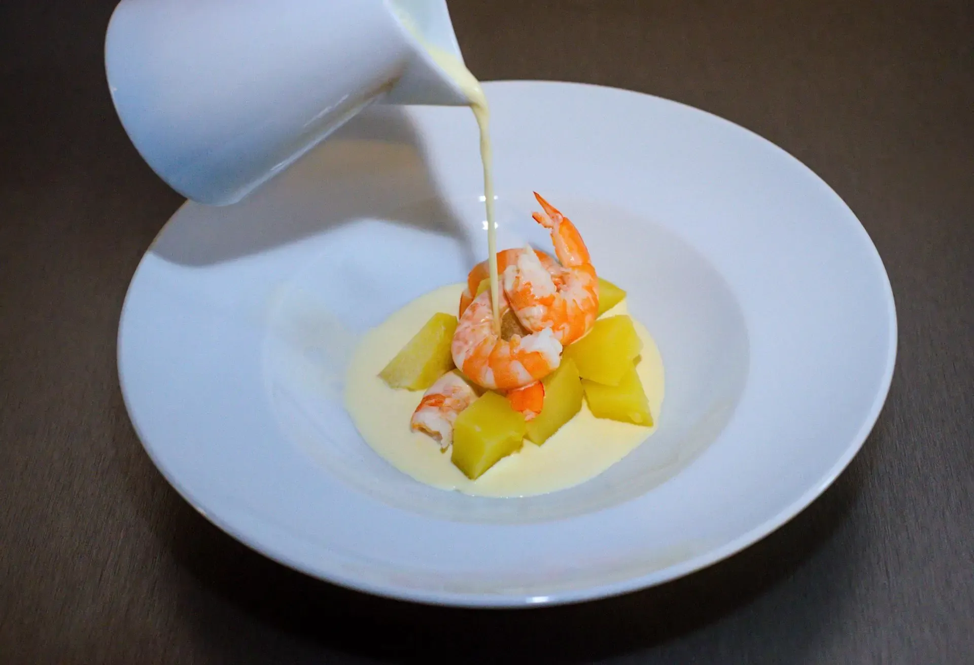 Gourmet shrimp dish served with creamy sauce and potatoes on a white plate.