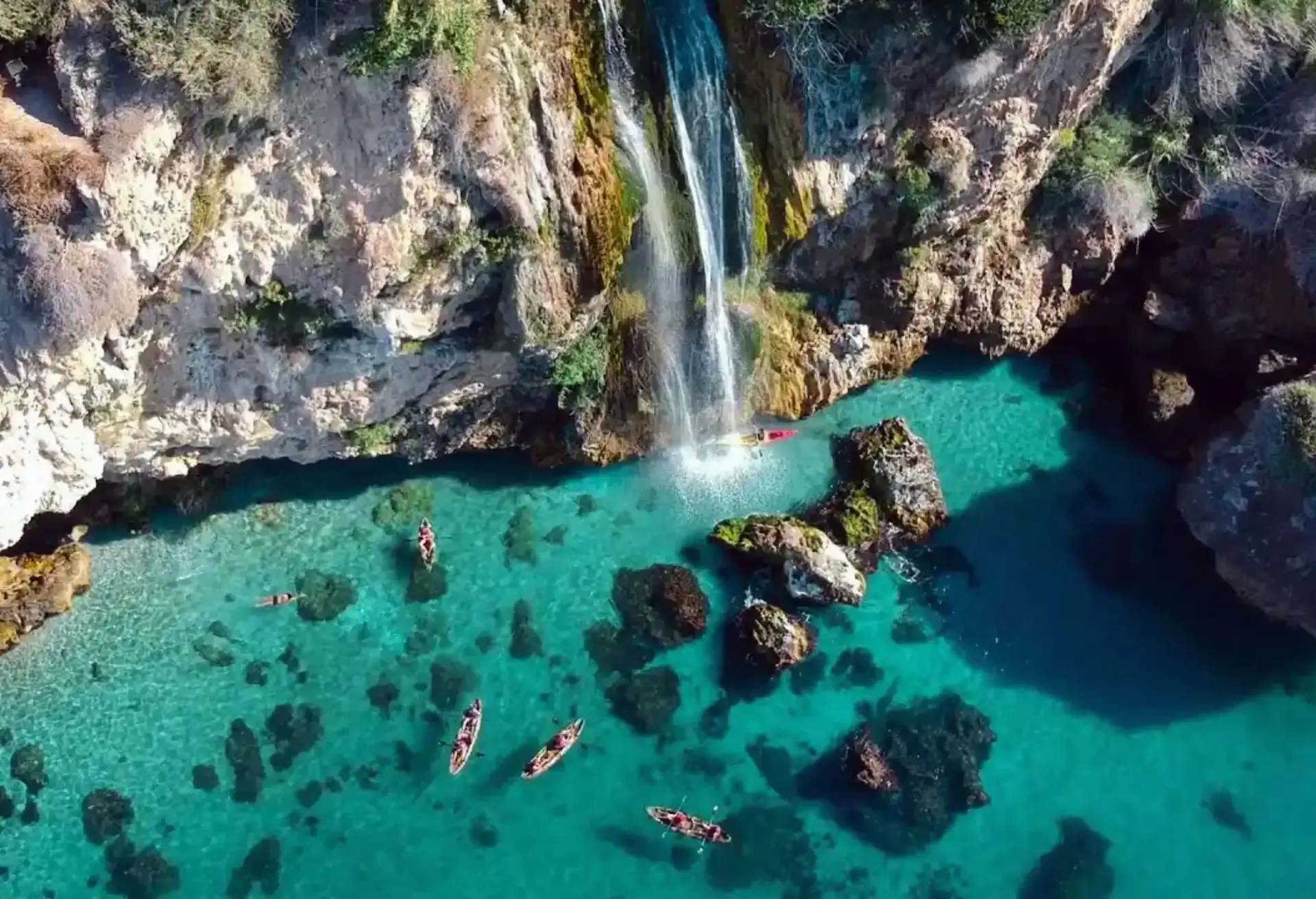 Waterfall cascading into crystal-clear turquoise waters surrounded by kayakers.