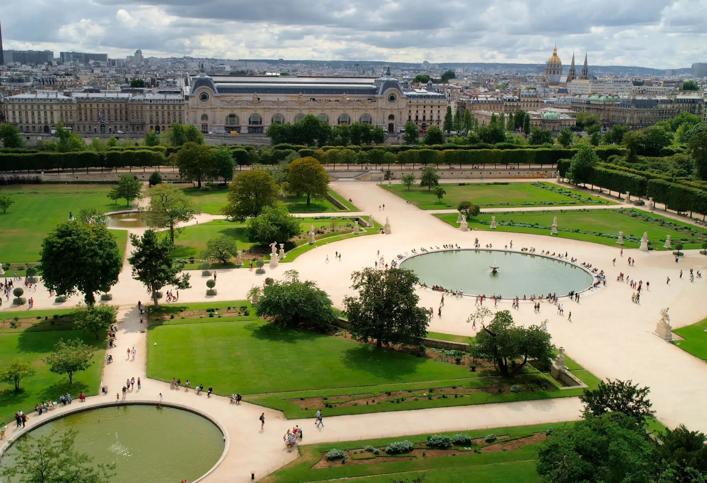 Lush green trees with a cityscape view in the background enclose a public garden with three ponds.