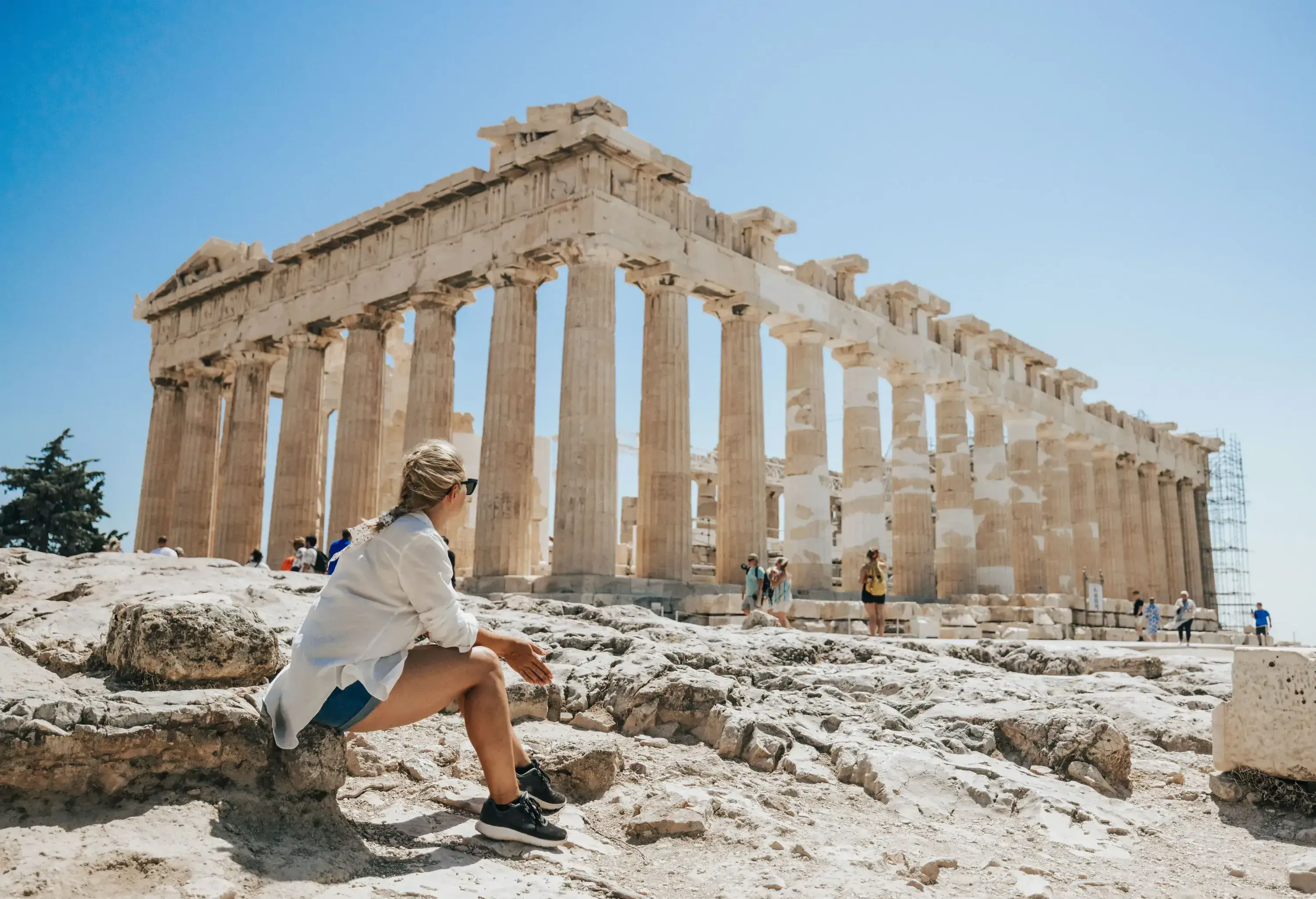 A woman sitting on a stone block looking at a majestic ancient temple on a bright day.