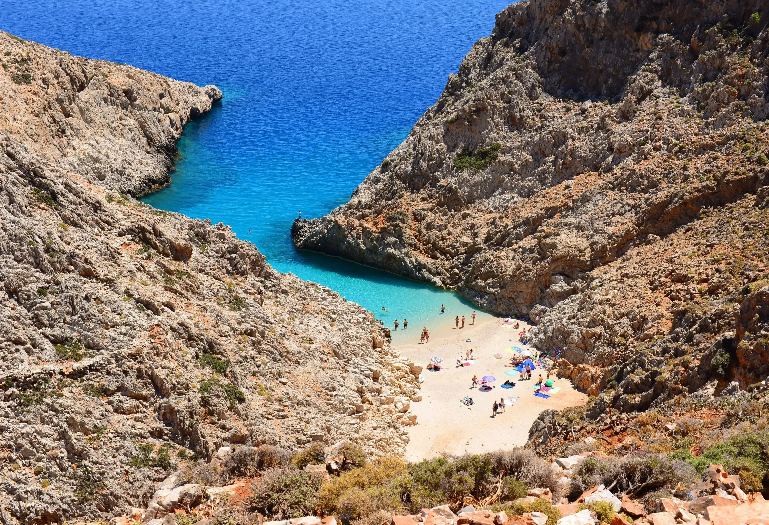 A crowded beach in a narrow cove surrounded by jagged slopes.