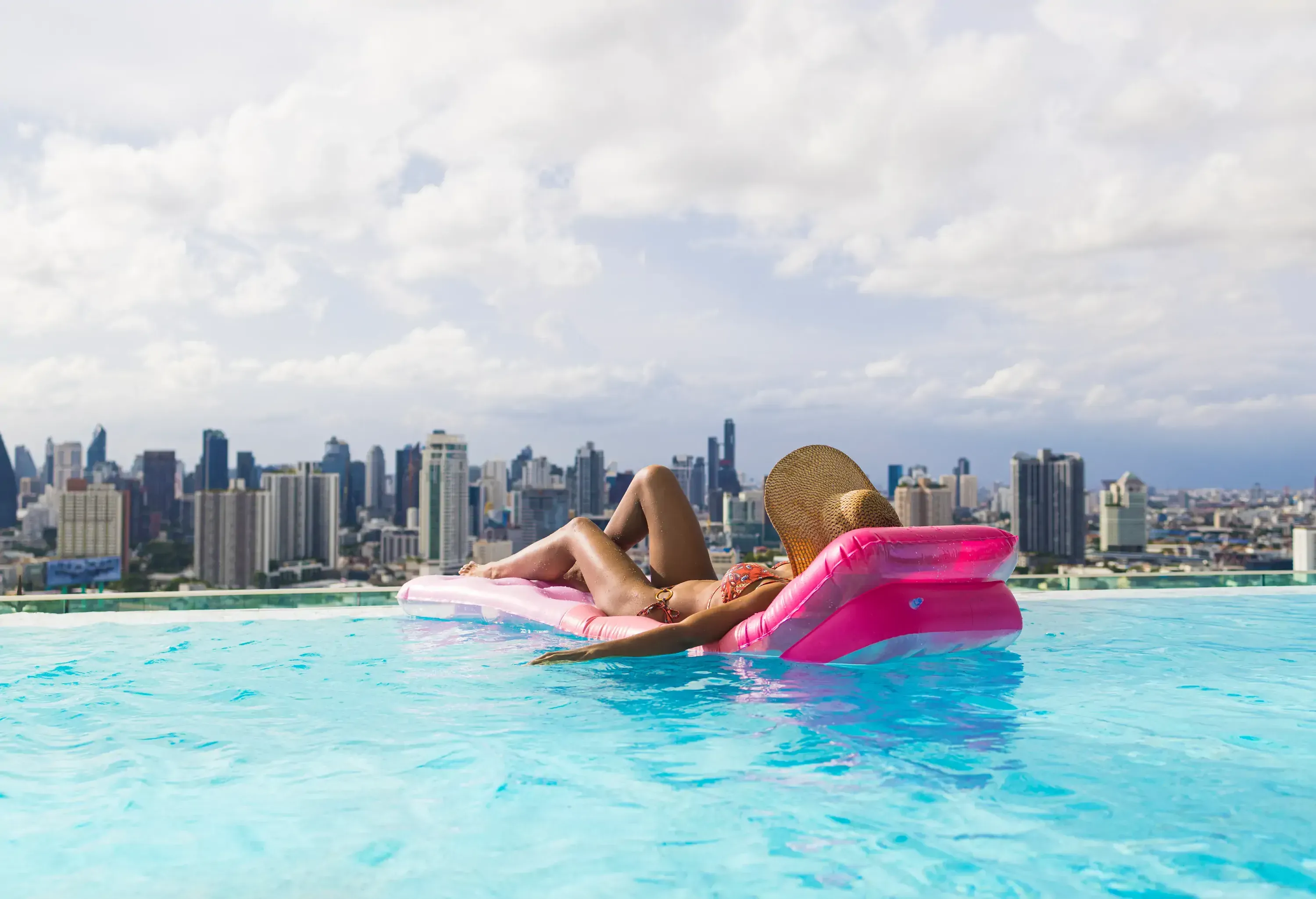 Sexy tanned skin woman sunbathing on Pool float mat in rooftop swimming pool of condominium in Bangkok City of Thailand , Happy young woman in bikini with rubber inflatable float , Urban Lifestyle concept