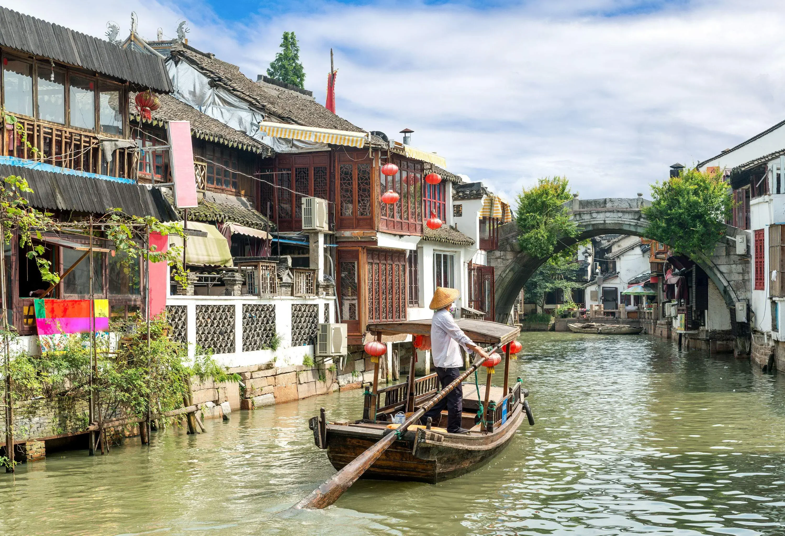 A man puddling a boat over a muddy lake surrounded by houses towards an arch.
