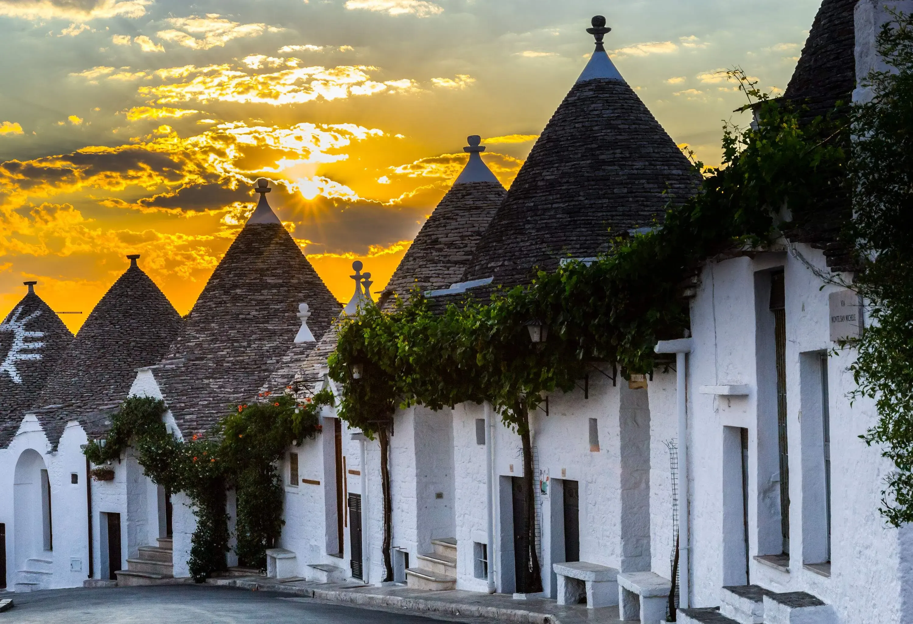 The blazing sun piercing through the clouds over the dry stone houses with cone-shaped roofs.