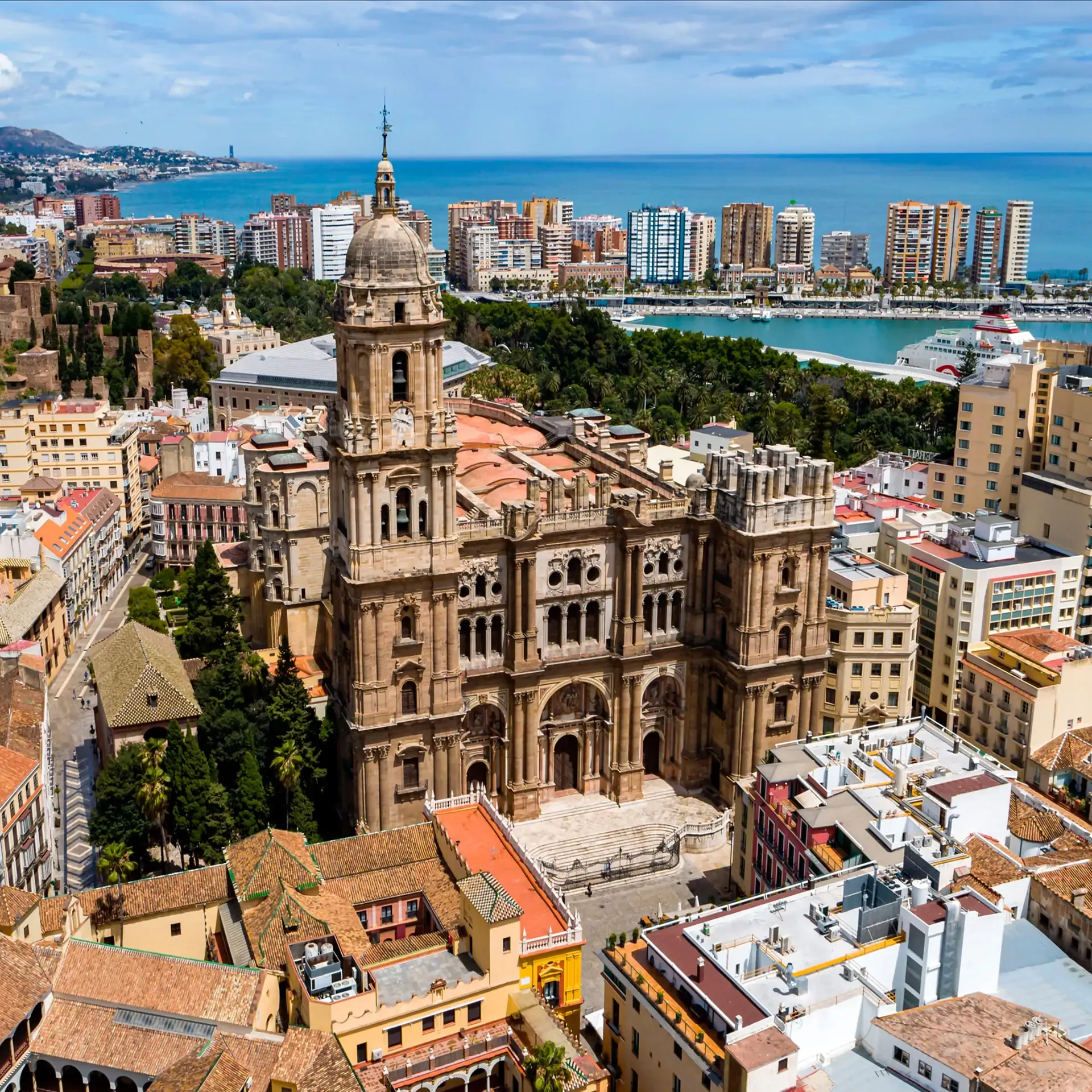 Aerial view of a historic cathedral with a tall tower in a coastal city by the blue ocean.