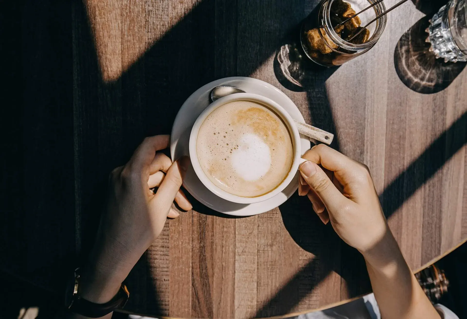 Top view of woman sitting by the window in coffee shop enjoying the warmth of sunlight and drinking coffee