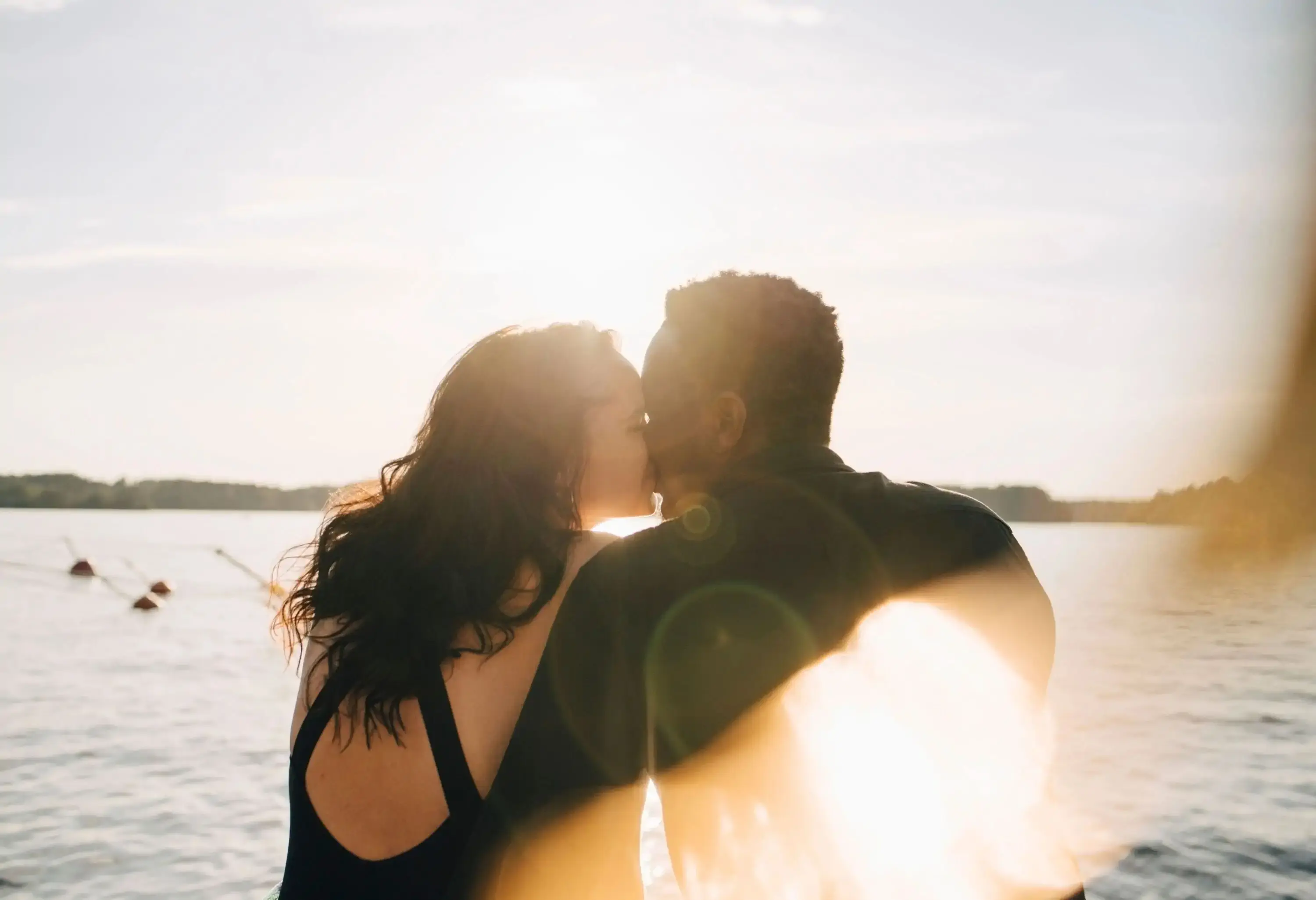 A romantic couple sharing a kiss as they sit by a lake.