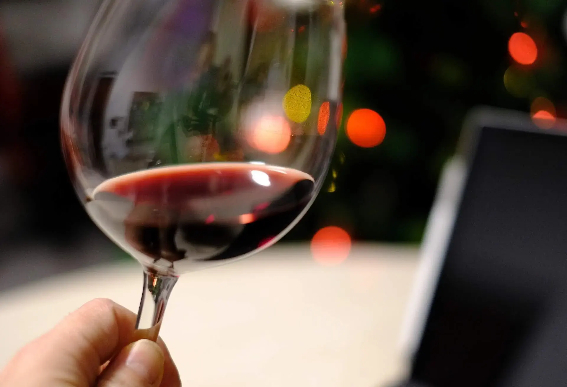 Partial section of a glass of red wine with illuminated Christmas lights in the background.