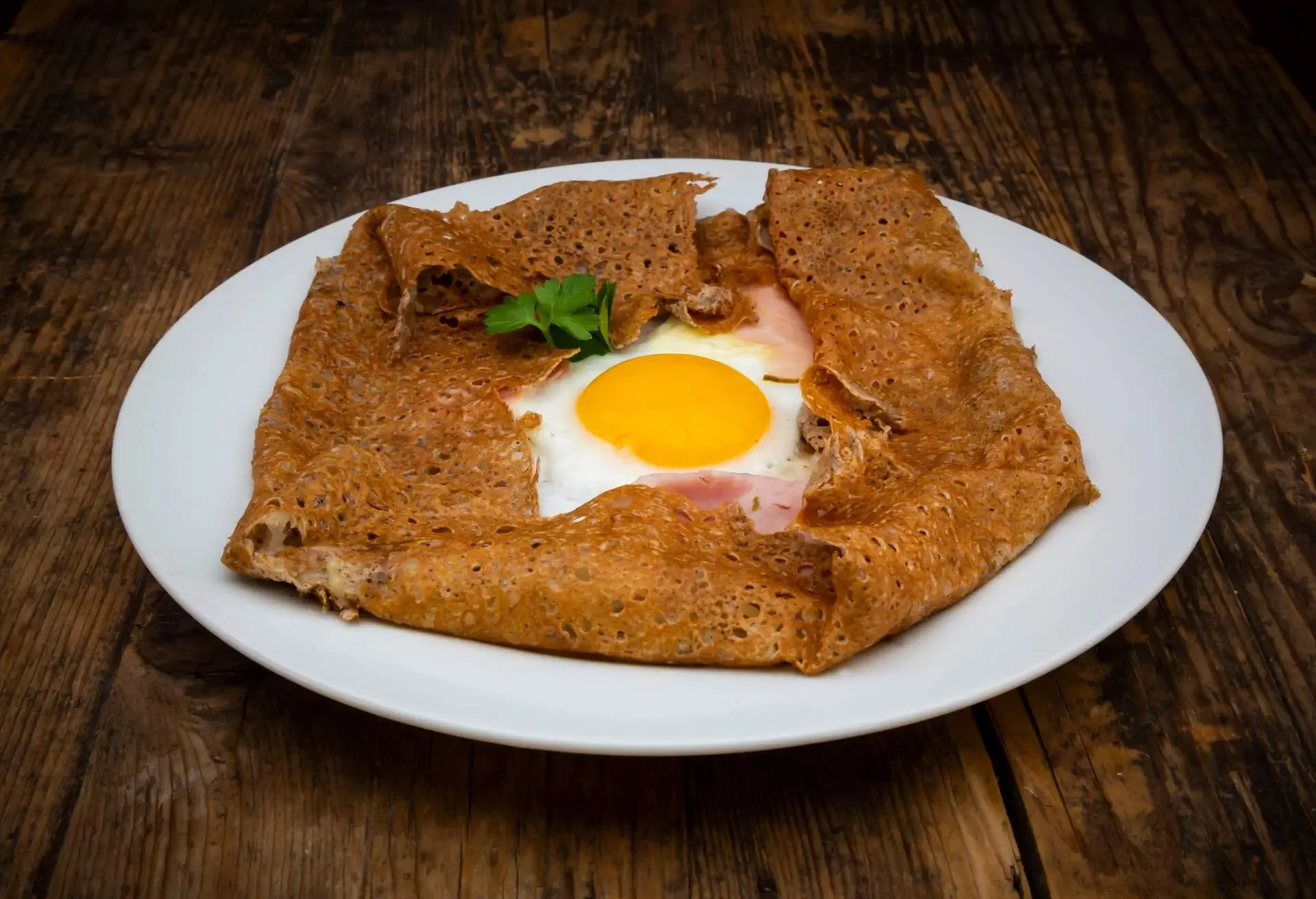 A ham and egg galette served in a white plate.