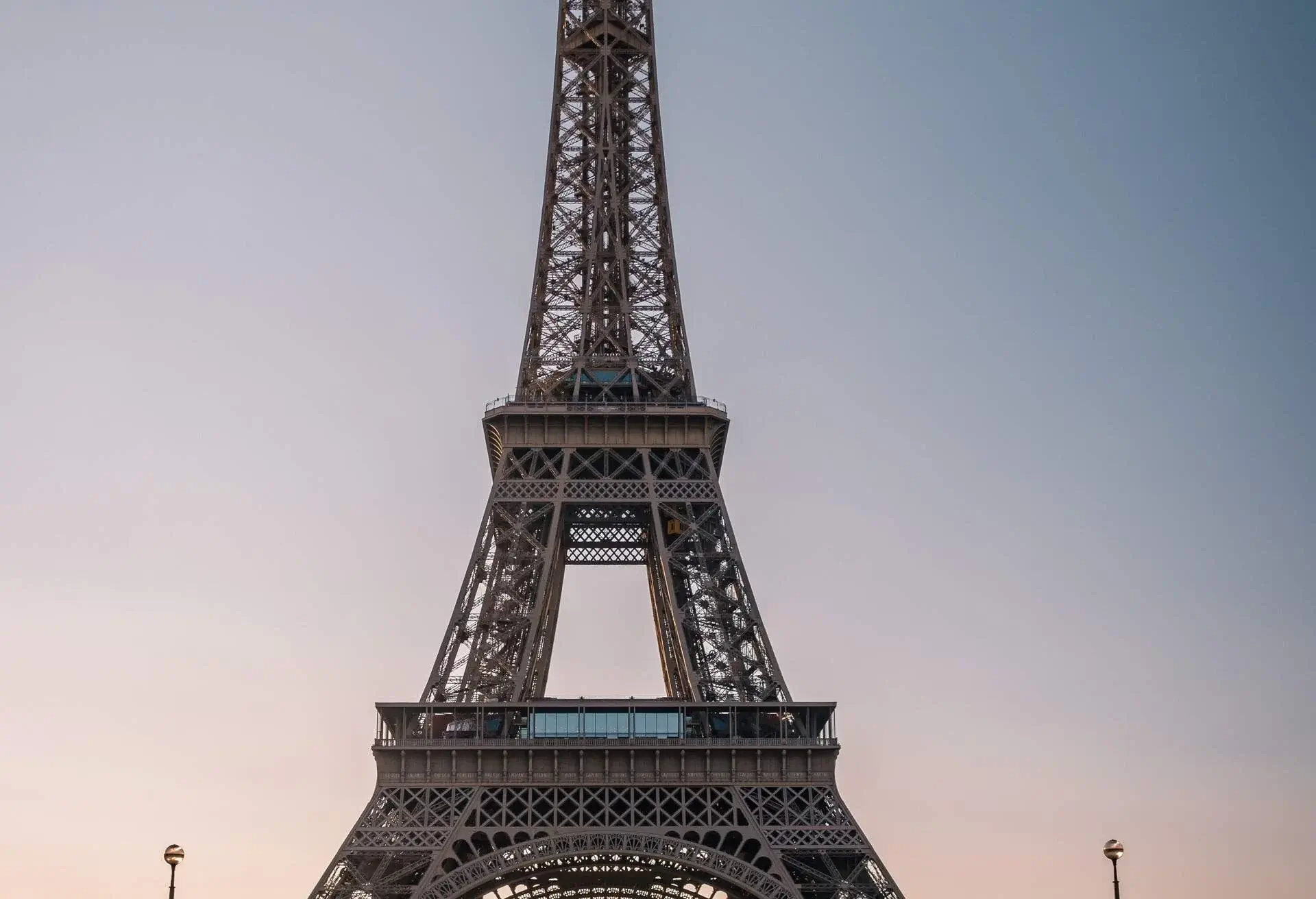 A person is holding a rainbow umbrella in the middle of the road under the Eiffel Tower.
