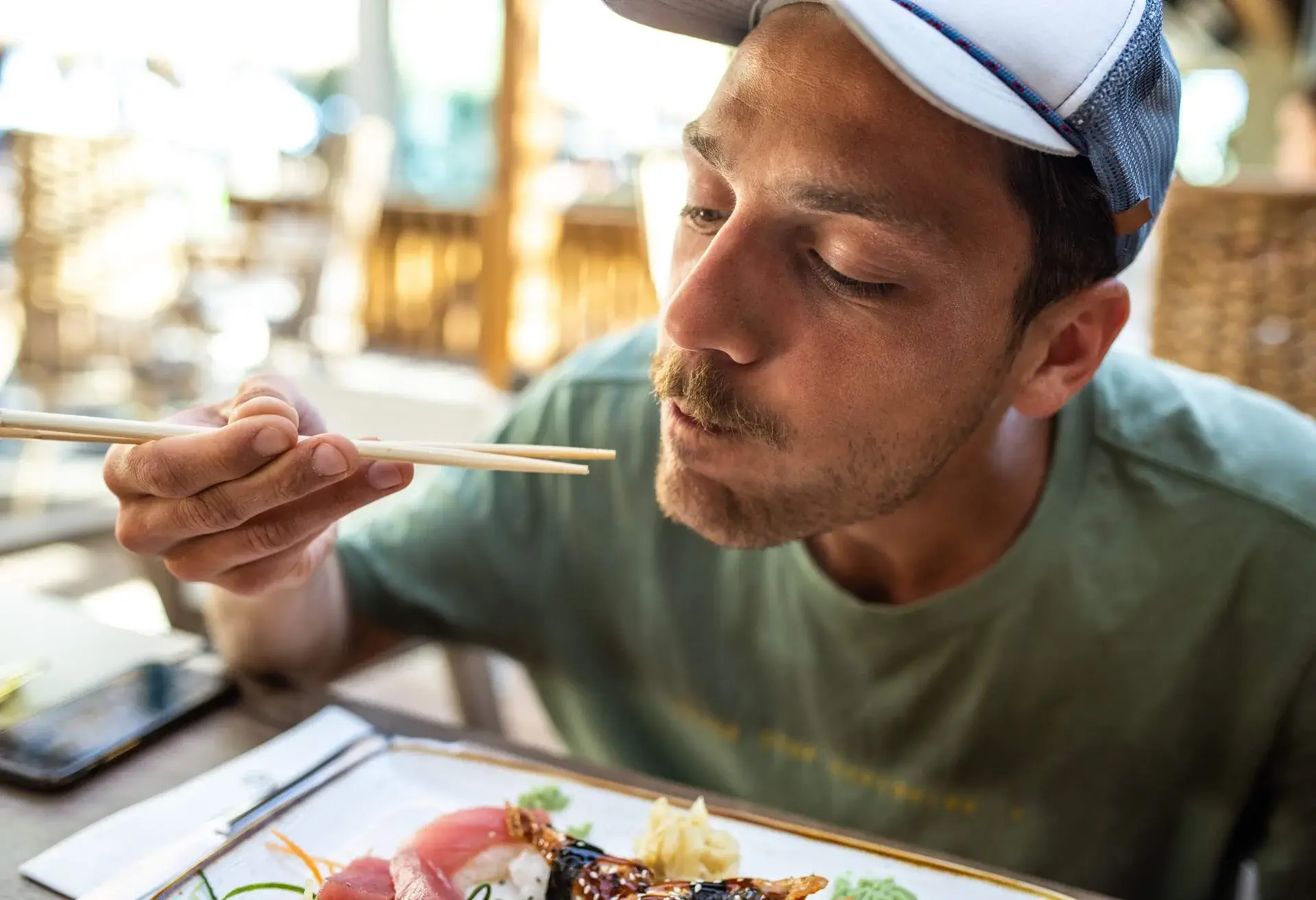 Young man eating delicious sushi with chopsticks at outdoor restaurant. Sashimi, nigiri, unagi sushi, tuna, salmon, wasabi